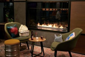 Die Lounge des Moxy Edinburgh Fountainbridge mit Kamin und dunkelgrünen Loungesesseln.