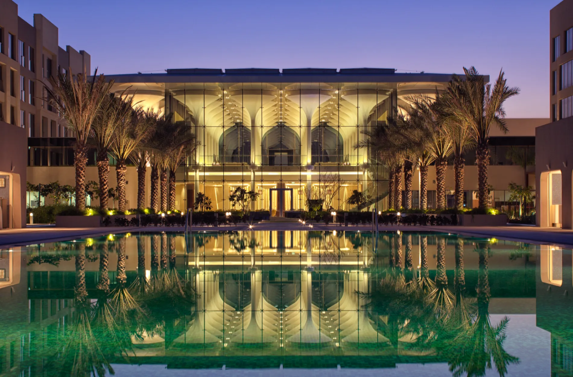 Der beleuchtete Außenpool des Kempinski Hotel Muscat mit Palmen.