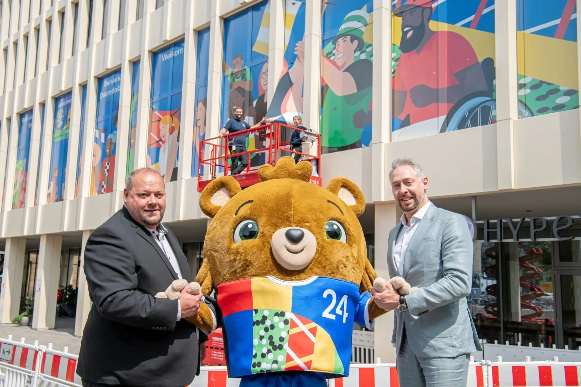 Willkommensgruß an der Fassade des Hyperion Hotel Leipzig. Hotelier Lars Ziegenhorn (links) und Stefan Schedler (rechts) mit UEFA EURO 2024 Maskottchen Albärt.