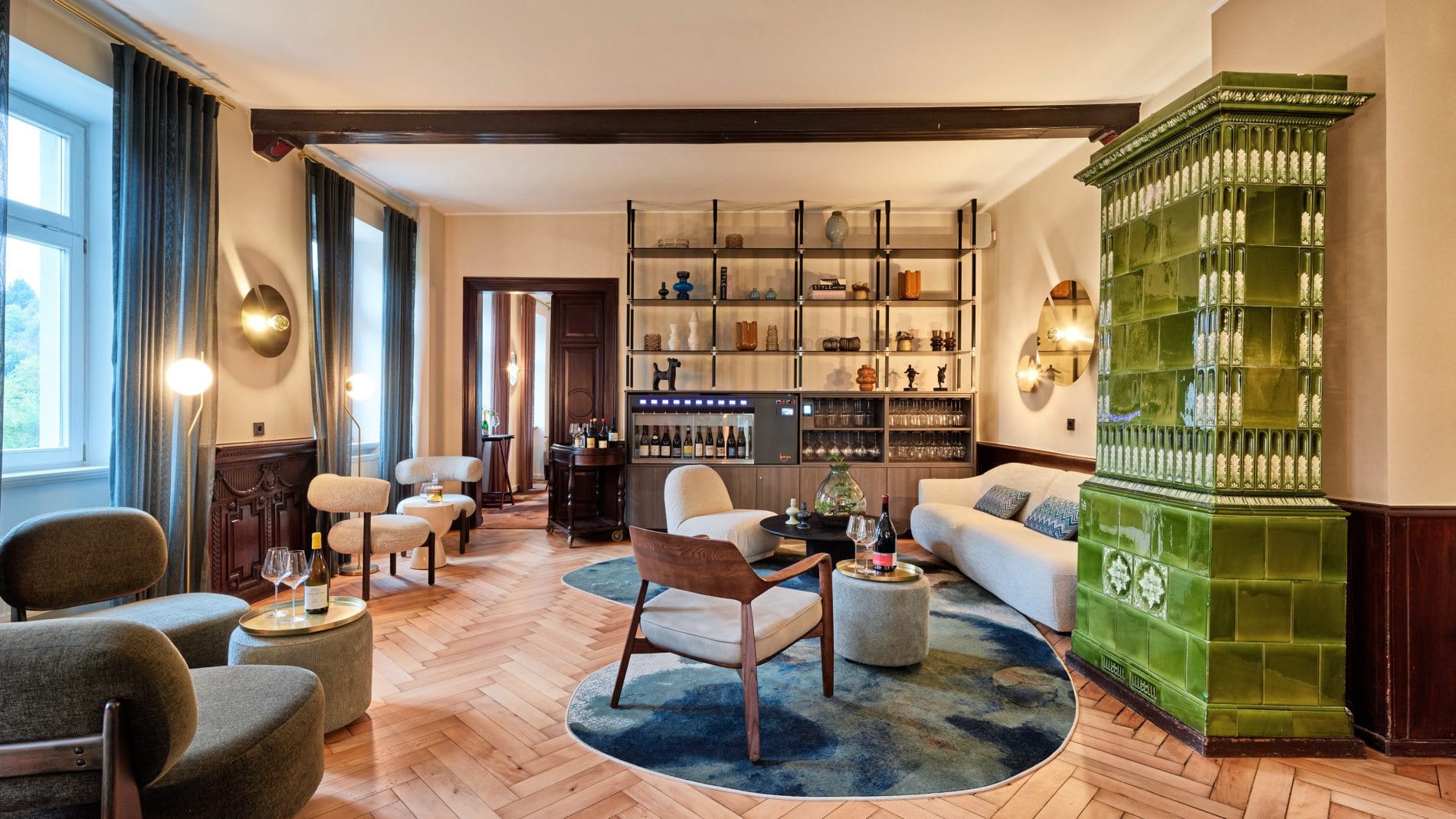 Lounge mit grünem Kachelofen, Weinkühlschrank, Regal, Designer-Sitzmöbeln und Fischgrätparkett