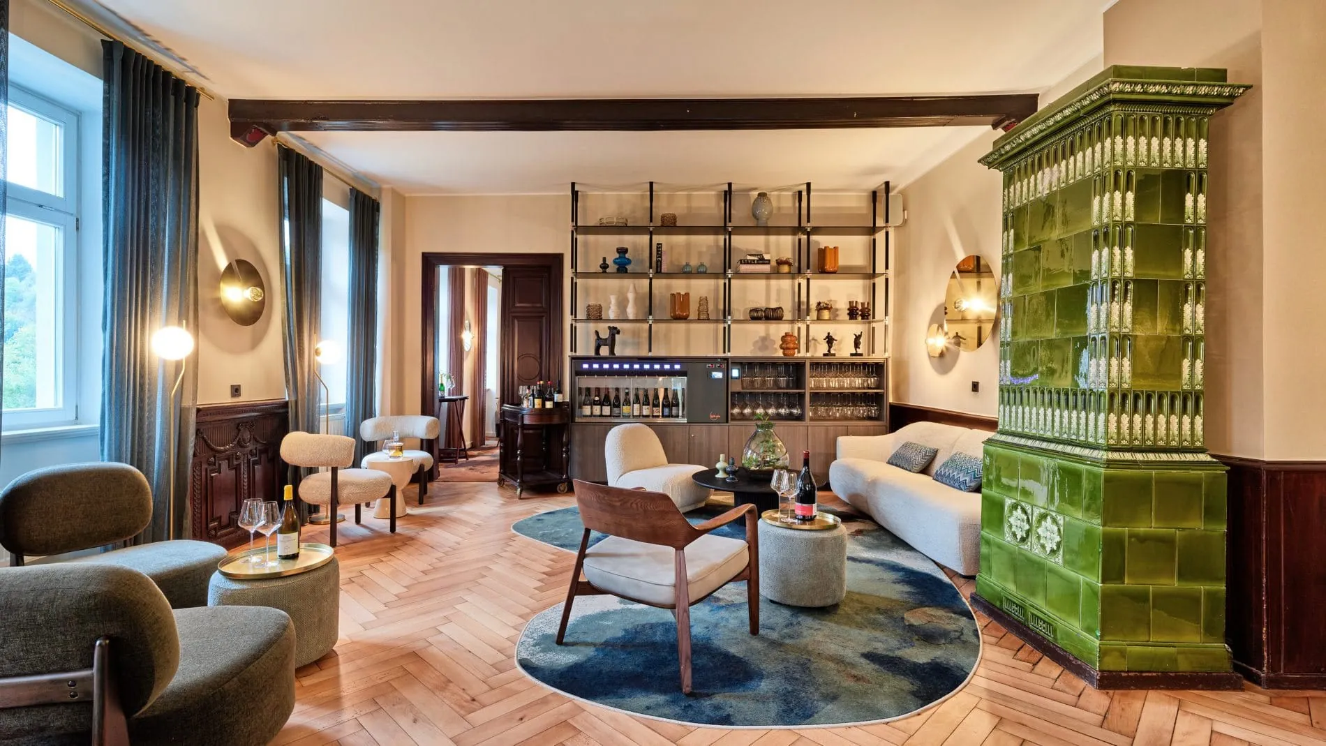 Lounge mit grünem Kachelofen, Weinkühlschrank, Regal, Designer-Sitzmöbeln und Fischgrätparkett