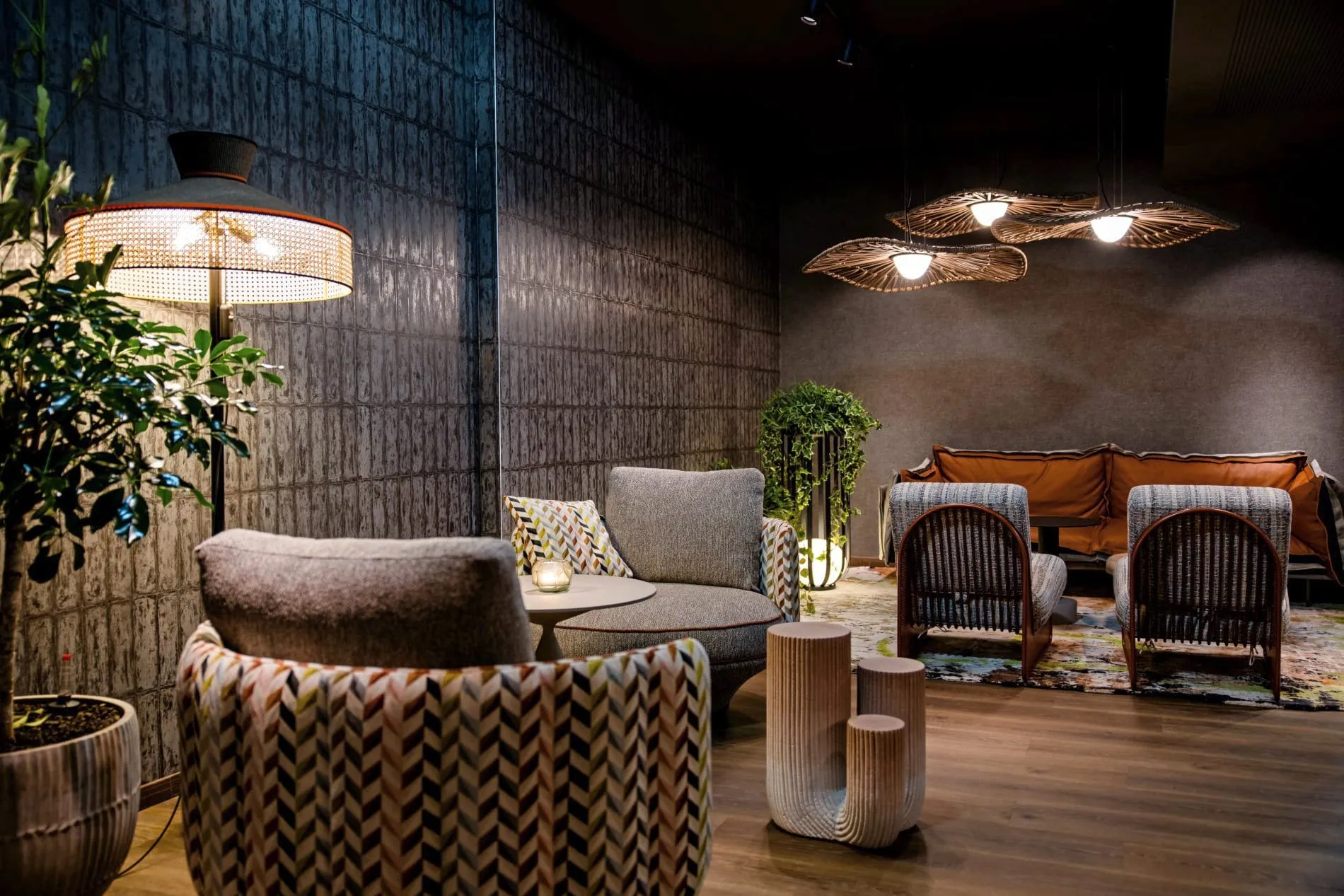 Dunkle Lounge-Ecke mit Rattansesseln, Designer-Pendelleuchten und gemustertem Teppich.