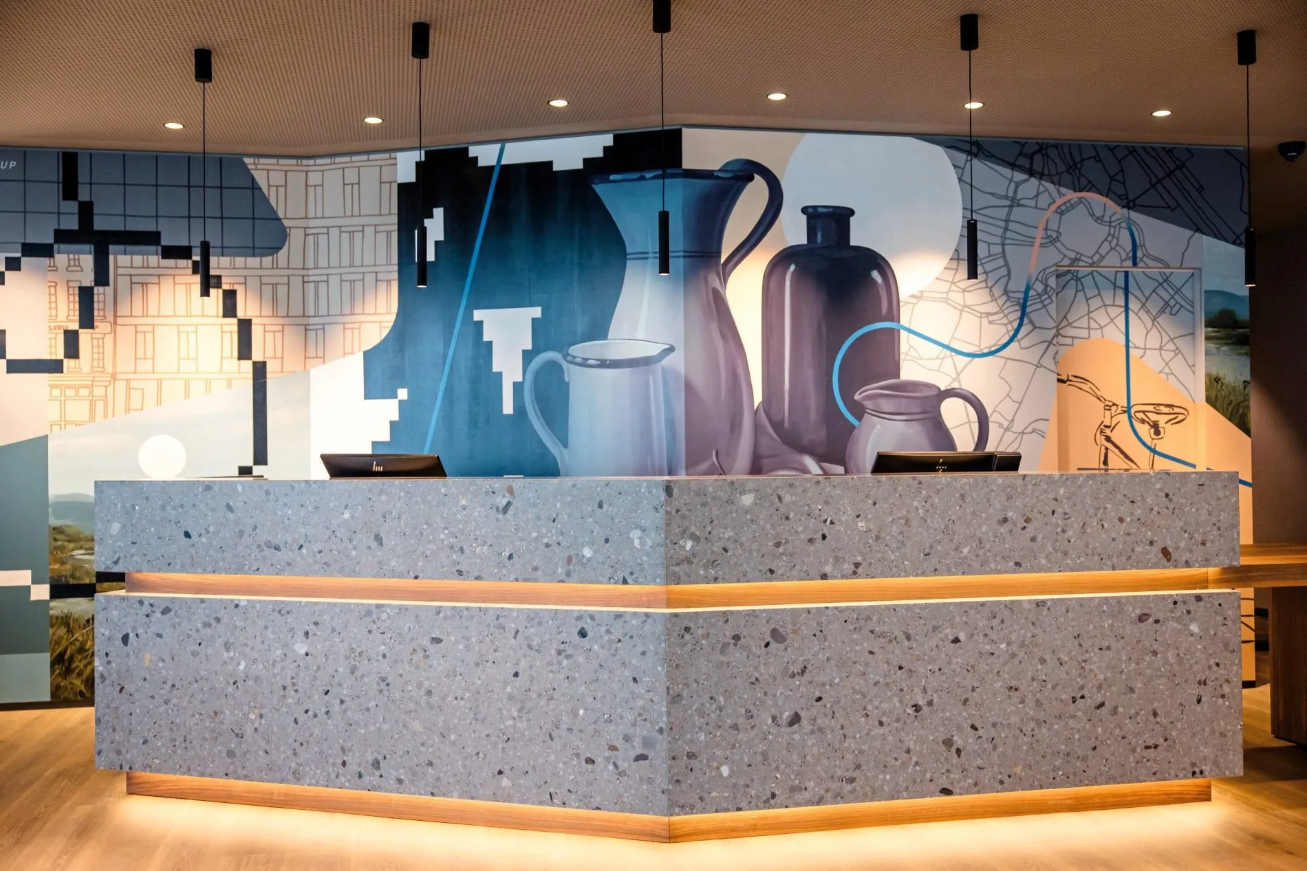 Hotelrezeption aus Terrazzo mit LED-Beleuchtung vor künstlerisch gestalteter Wand mit Vasen und Stadtmotiven.