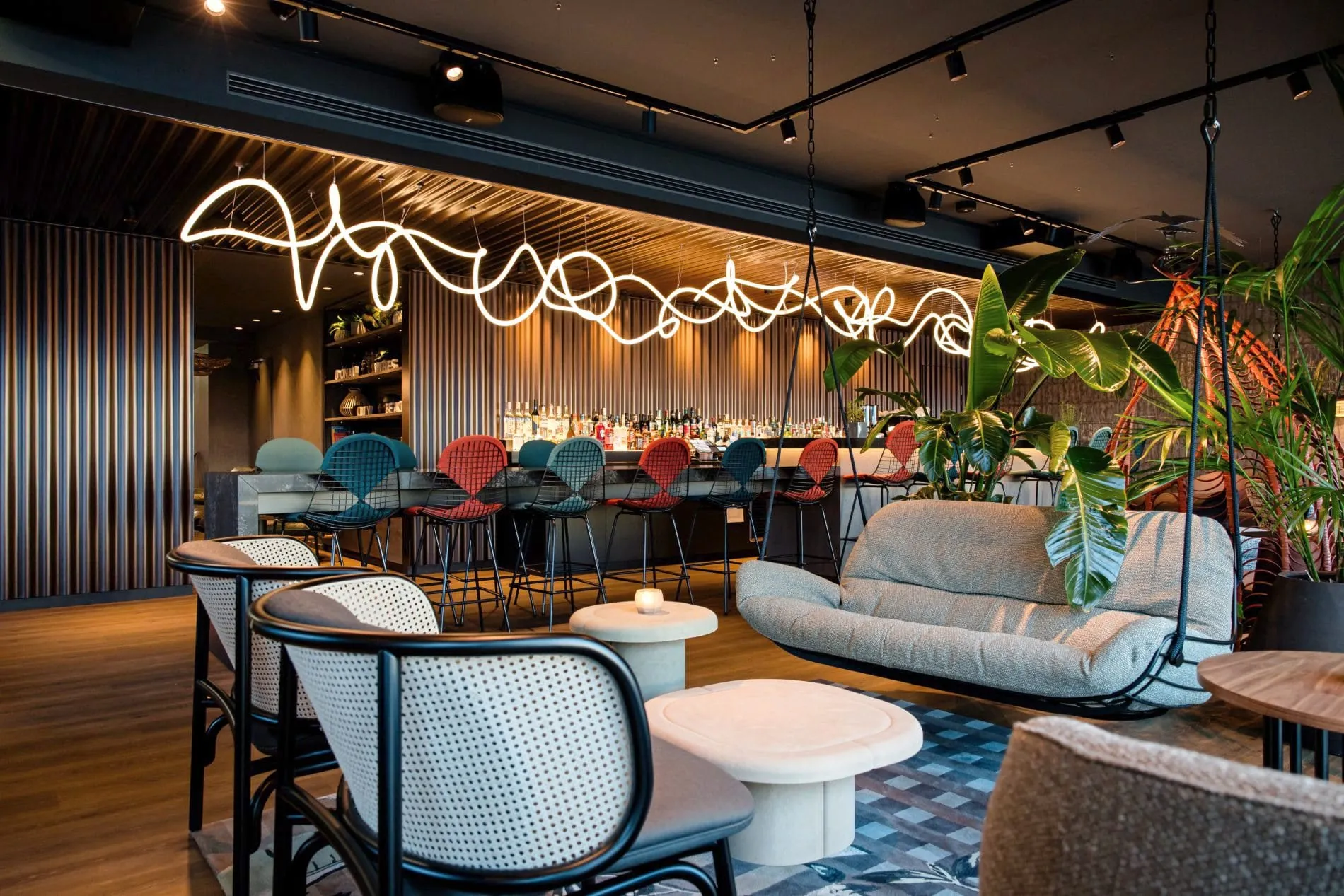 Moderne Hotelbar mit Neon-Lichtkunst, Bar, bunten Sesseln und tropischen Pflanzen.