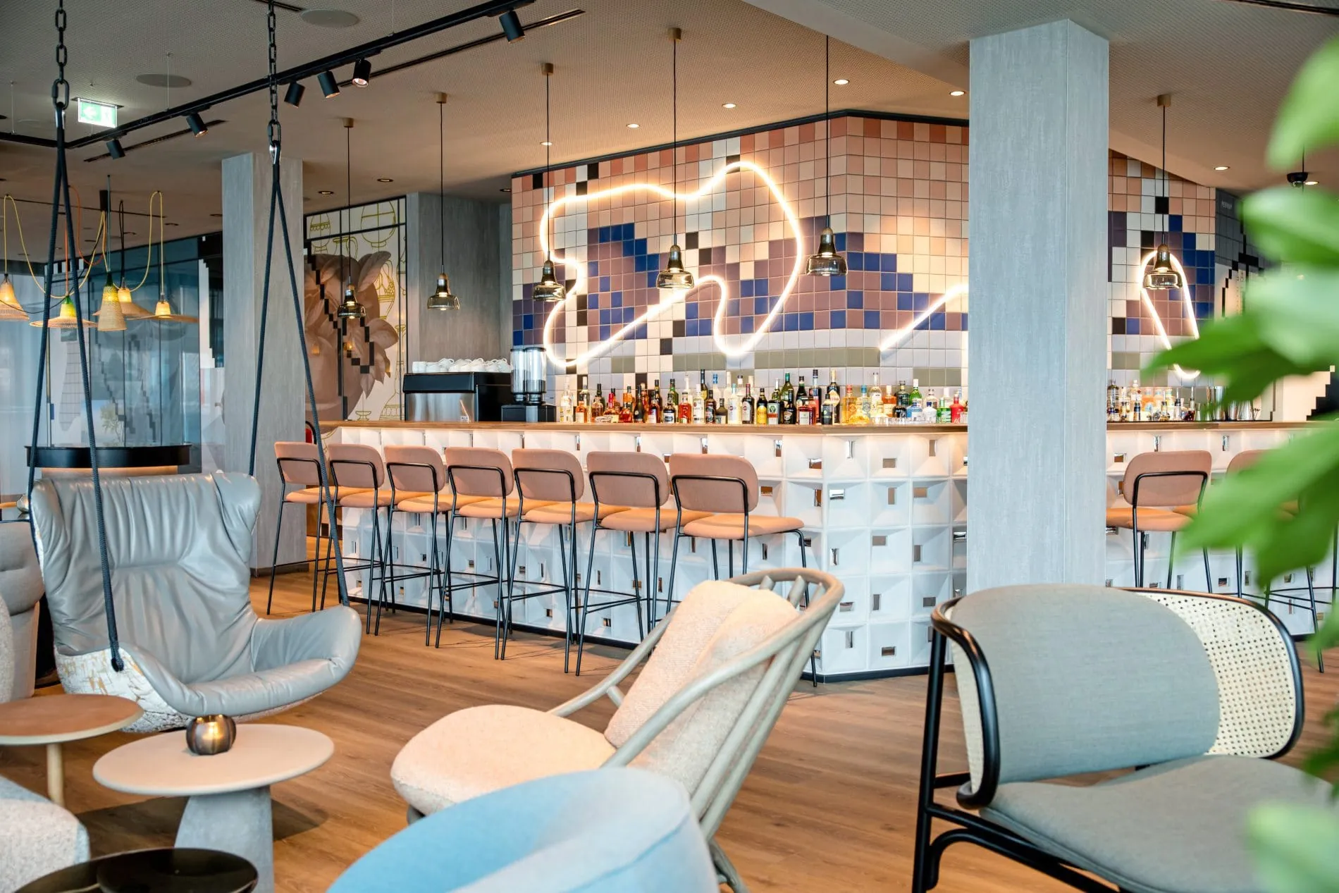 Hotelbar mit weißer Neon-Lichtkunst, bunten Barhockern und Pixel-Wandmuster im Hintergrund.