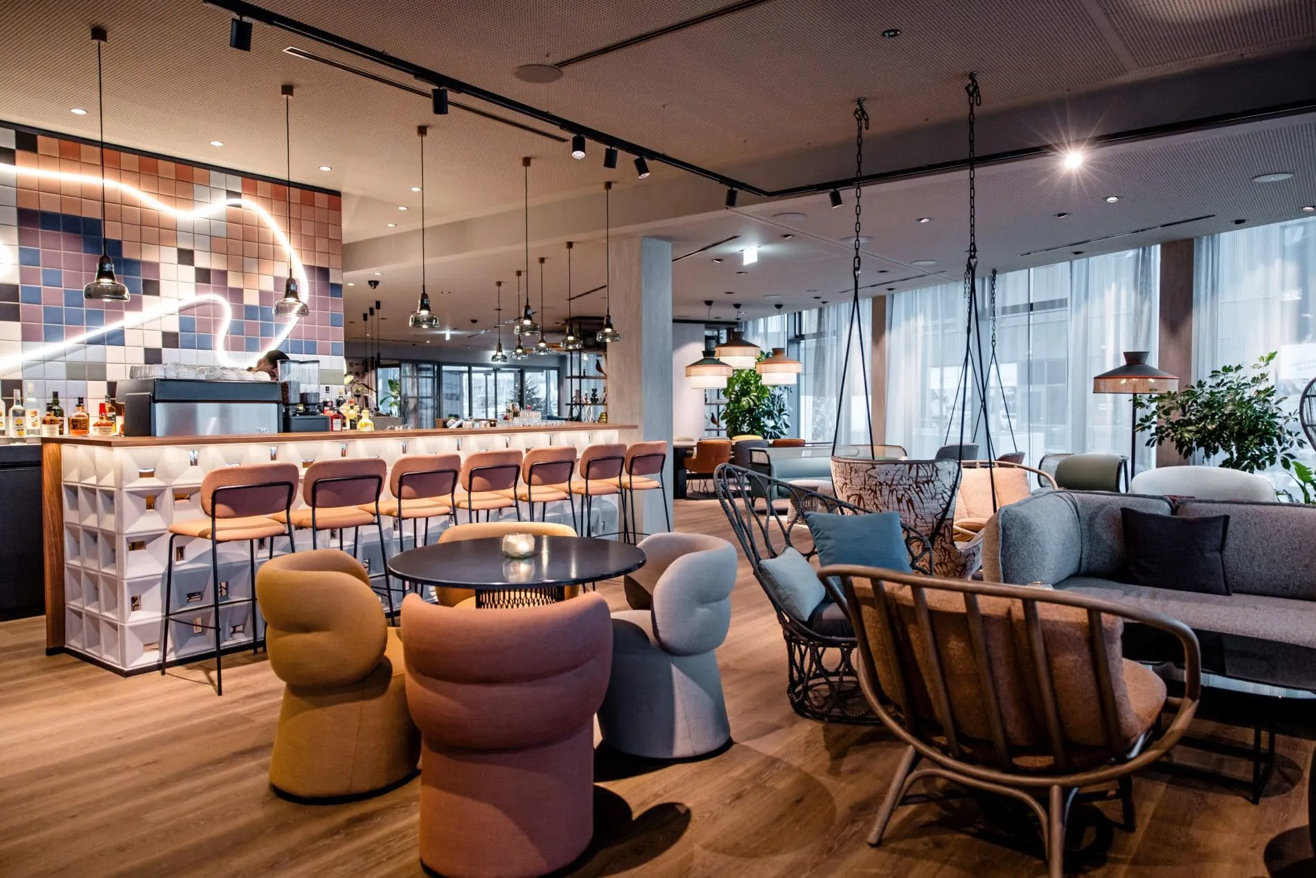 Moderne Hotellobby mit bunten Sesseln, Hängeschaukeln, Bartresen und Pixel-Wandkunst im Hintergrund.