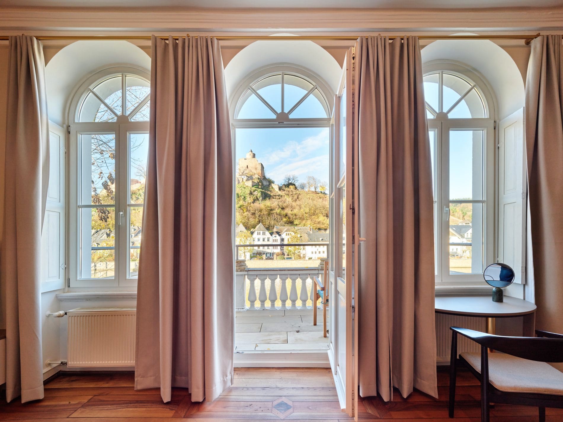 Drei Rundbogenfenster mit Balkonzugang und Ausblick auf historisches Gebäude auf Hügel