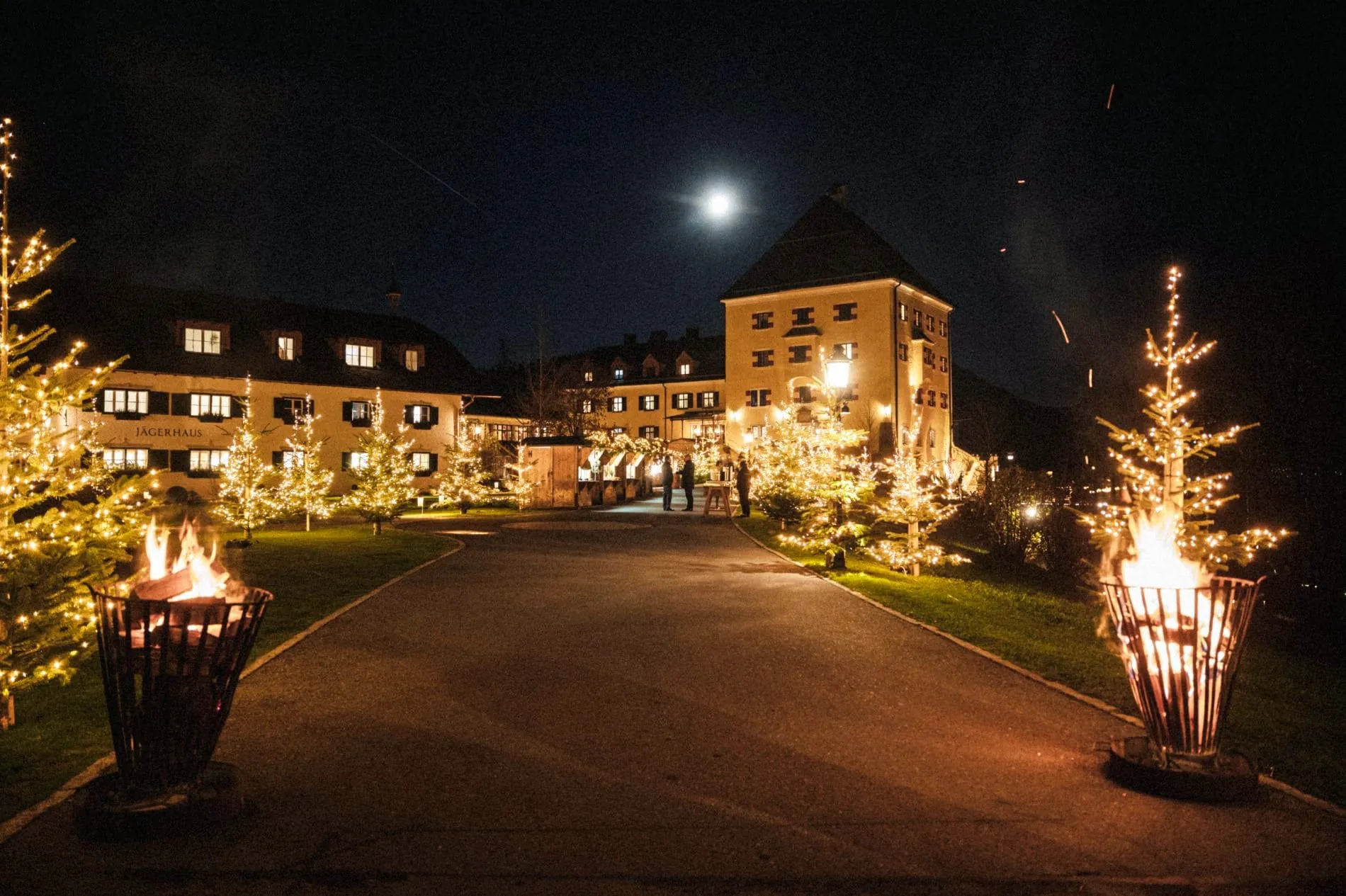 Weihnachtlich beleuchtetes Rosewood Schloss Fuschl mit Lichterketten, Feuerkörben und festlicher Dekoration bei Nacht.