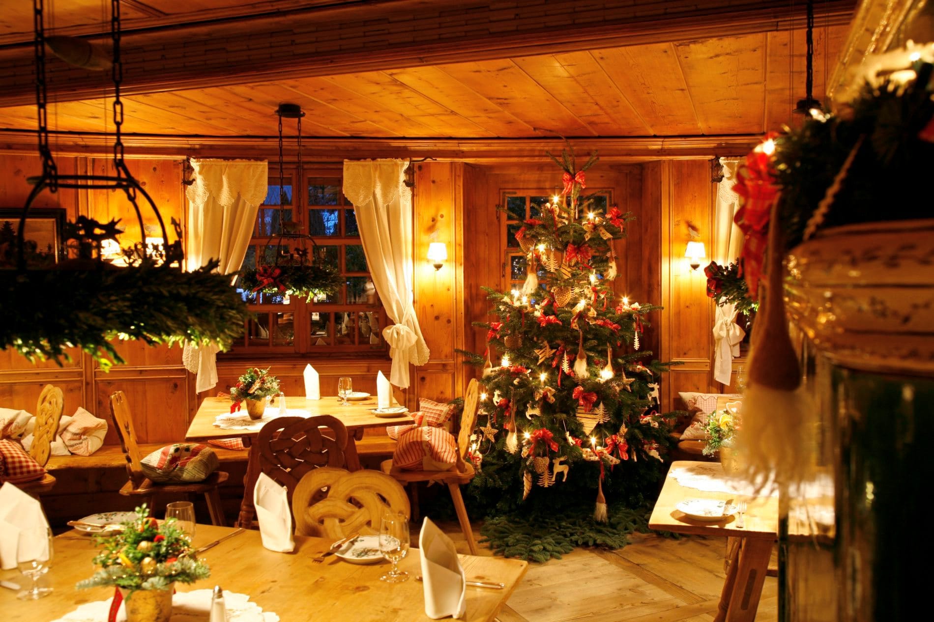 Weihnachtlich dekorierte Dorfstube mit Christbaum, Holzvertäfelung und festlich gedeckten Tischen im Hotel Bareiss.