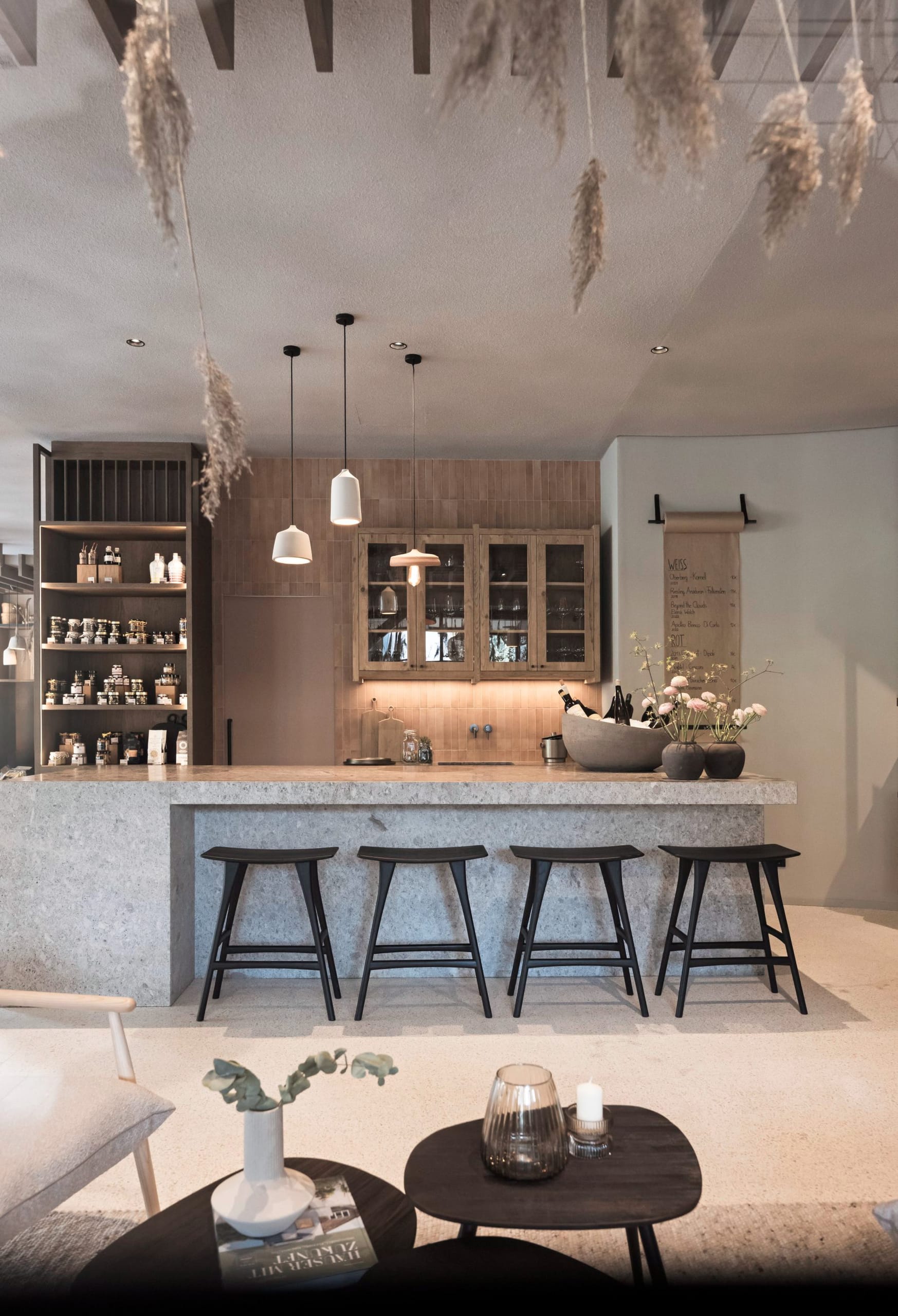 Bartresen aus Stein mit Hockern, Holzschränken und hängendem Pampasgras.