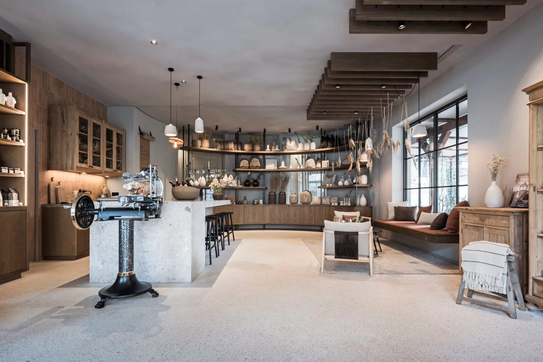 Offener Raum mit Steintresen, antiker Aufschnittmaschine, Regalen und Lounge-Bereich.
