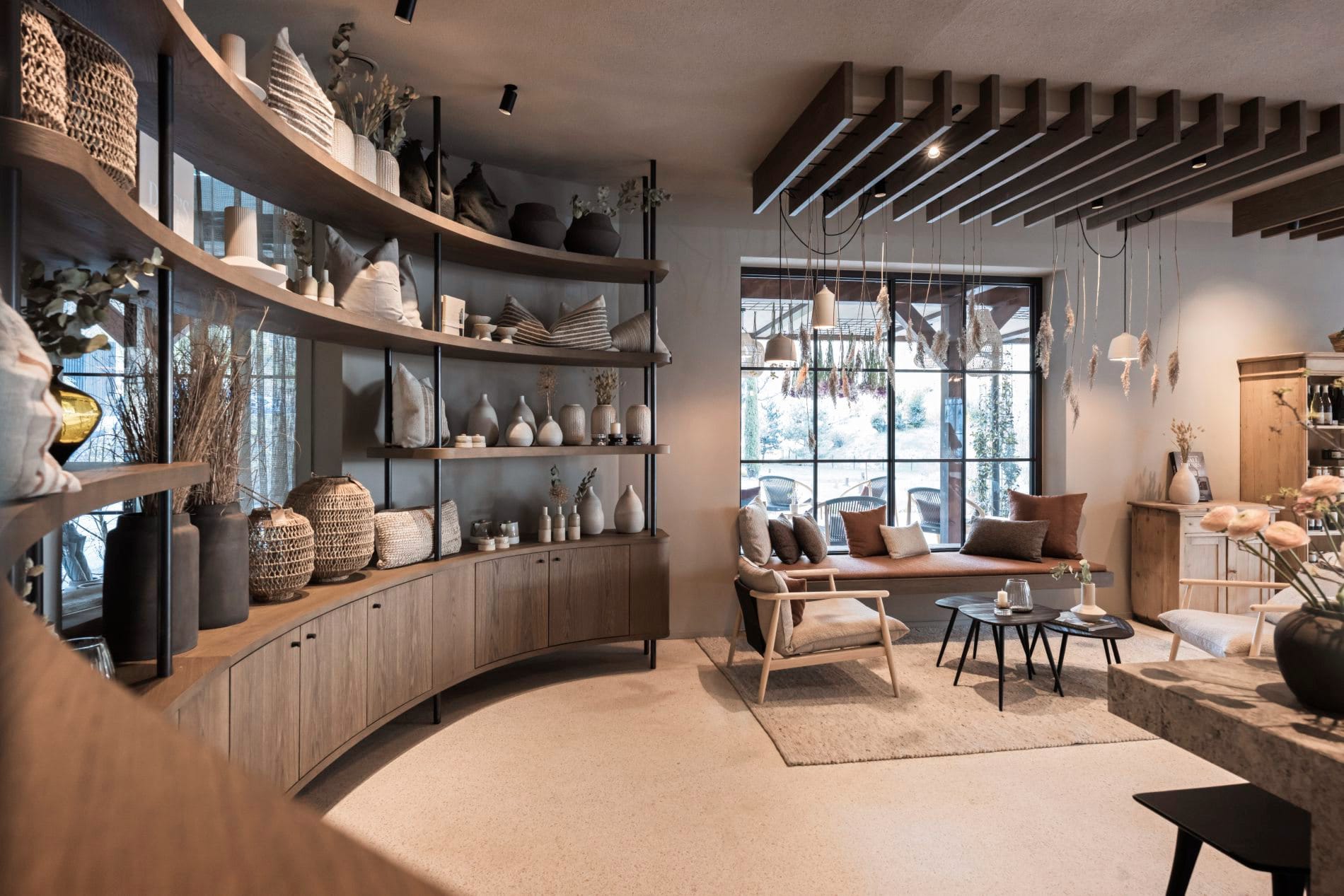 Geschwungenes Holzregal mit Vasen, Kissen und Körben in Erdtönen, Sitzbank im Hintergrund.