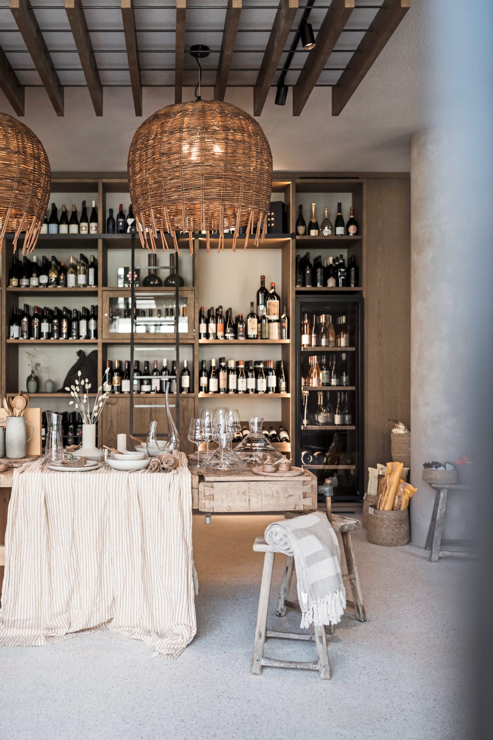 Offener Concept Store mit Weinregalen, Holztischen, Rattanleuchten und Dekoobjekten.