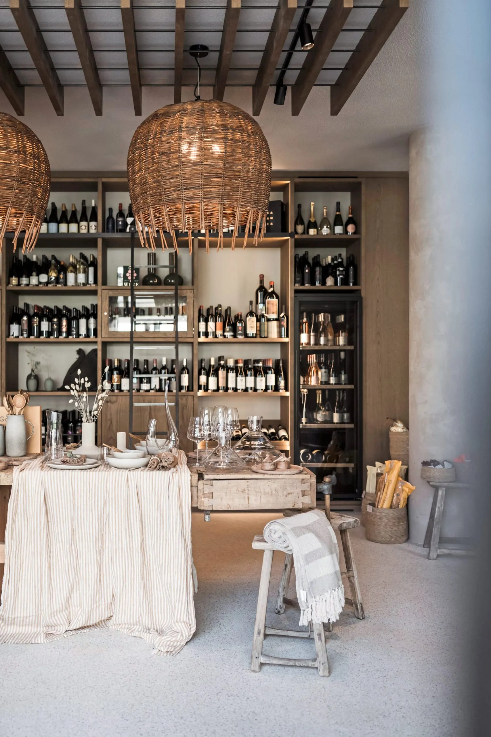 Offener Concept Store mit Weinregalen, Holztischen, Rattanleuchten und Dekoobjekten.