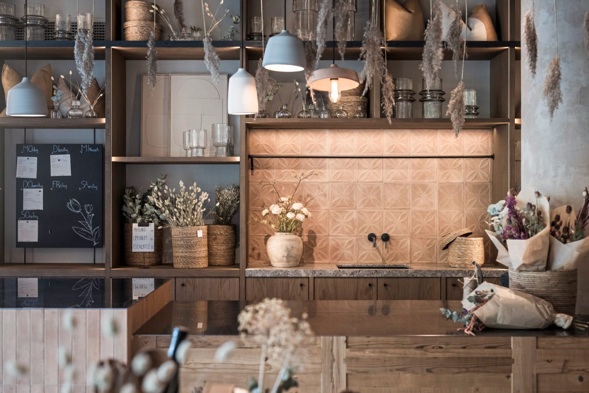 Holzregal mit Gläsern, Vasen und Trockenblumen, Terrakotta-Rückwand.