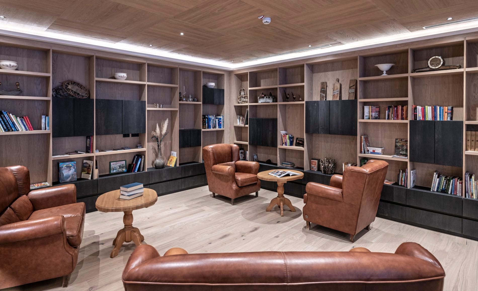 Elegante Lounge mit cognacfarbenen Ledersesseln und deckenhohen Holzregalen.