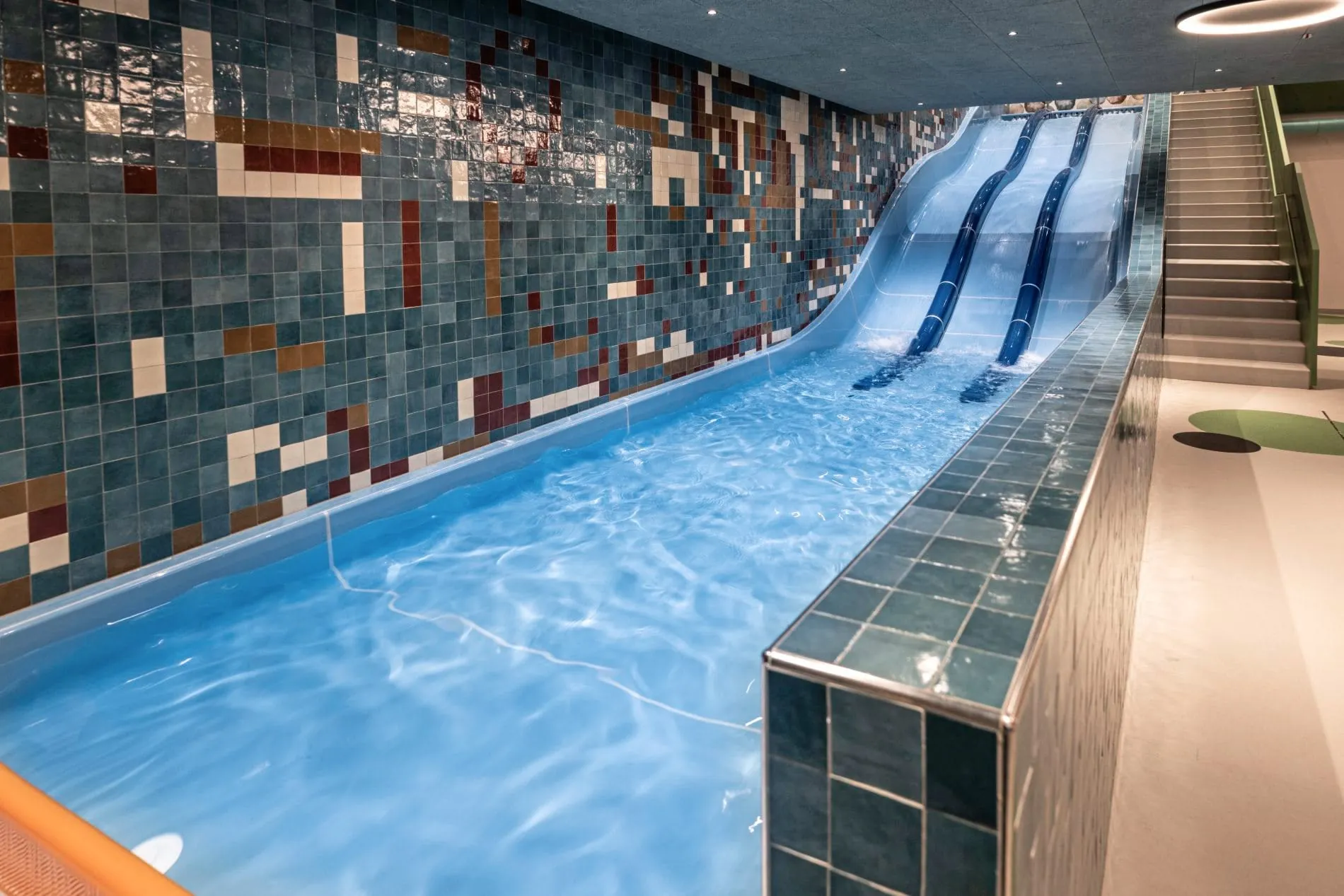 Kinderpool mit doppelter Wasserrutsche und buntem Fliesenmosaik im Family-Spa.