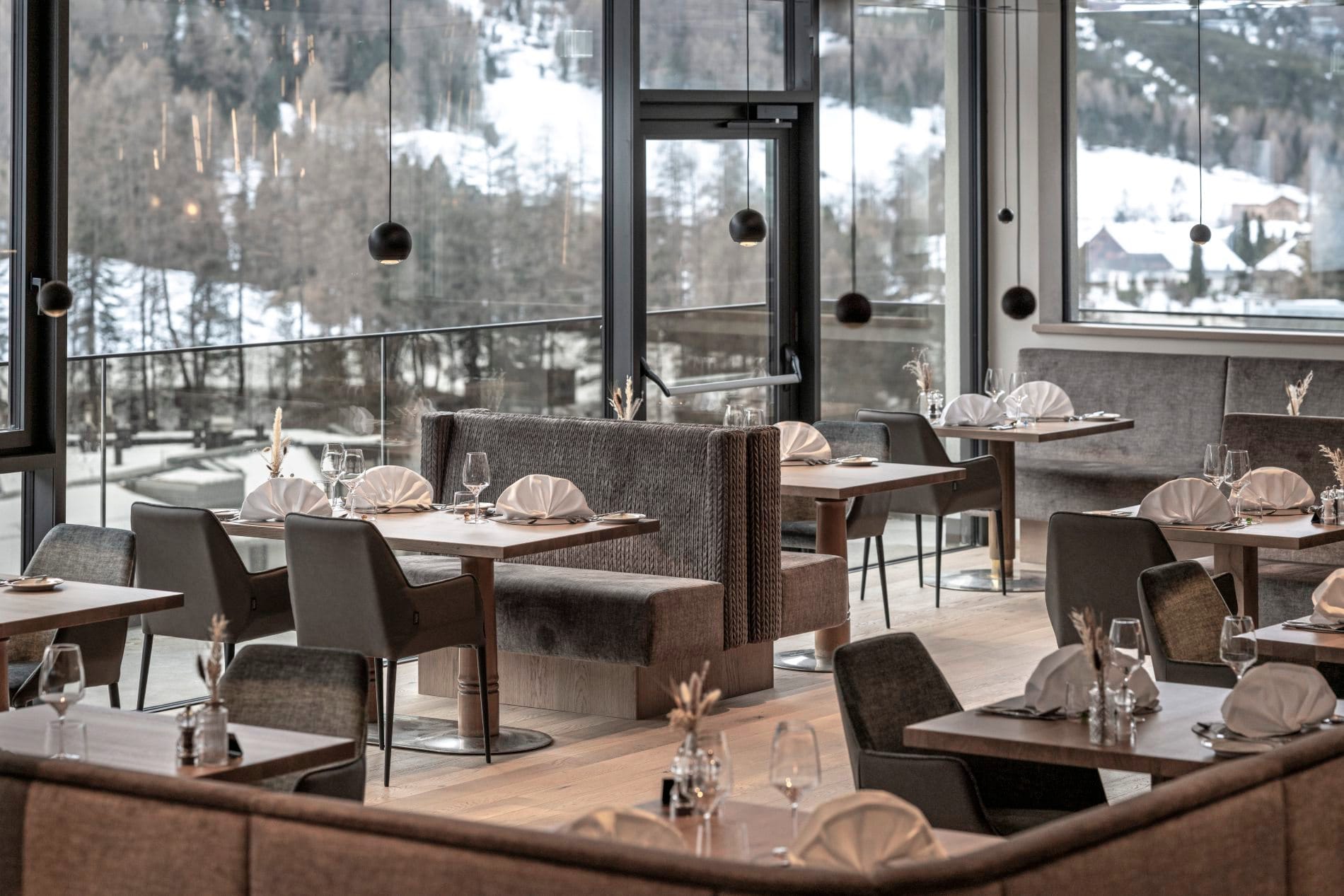Hotelrestaurant mit gedeckten Tischen, Sitzbänken und Panoramafenstern.