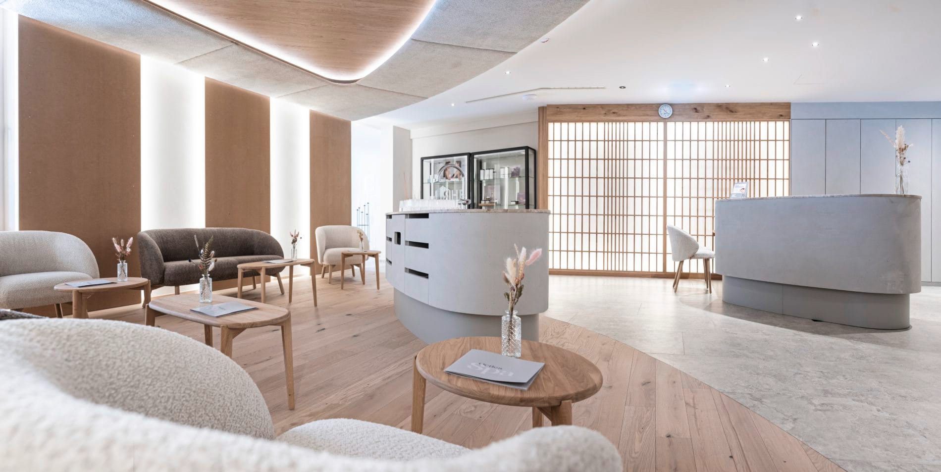 Spa-Rezeption mit geschwungenem Tresen, Loungesesseln und Holzakzenten.