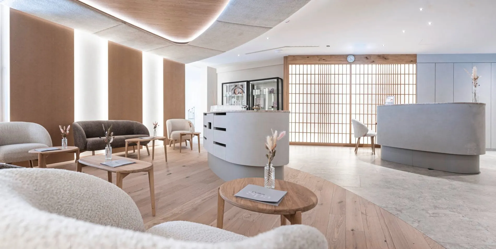 Spa-Rezeption mit geschwungenem Tresen, Loungesesseln und Holzakzenten.