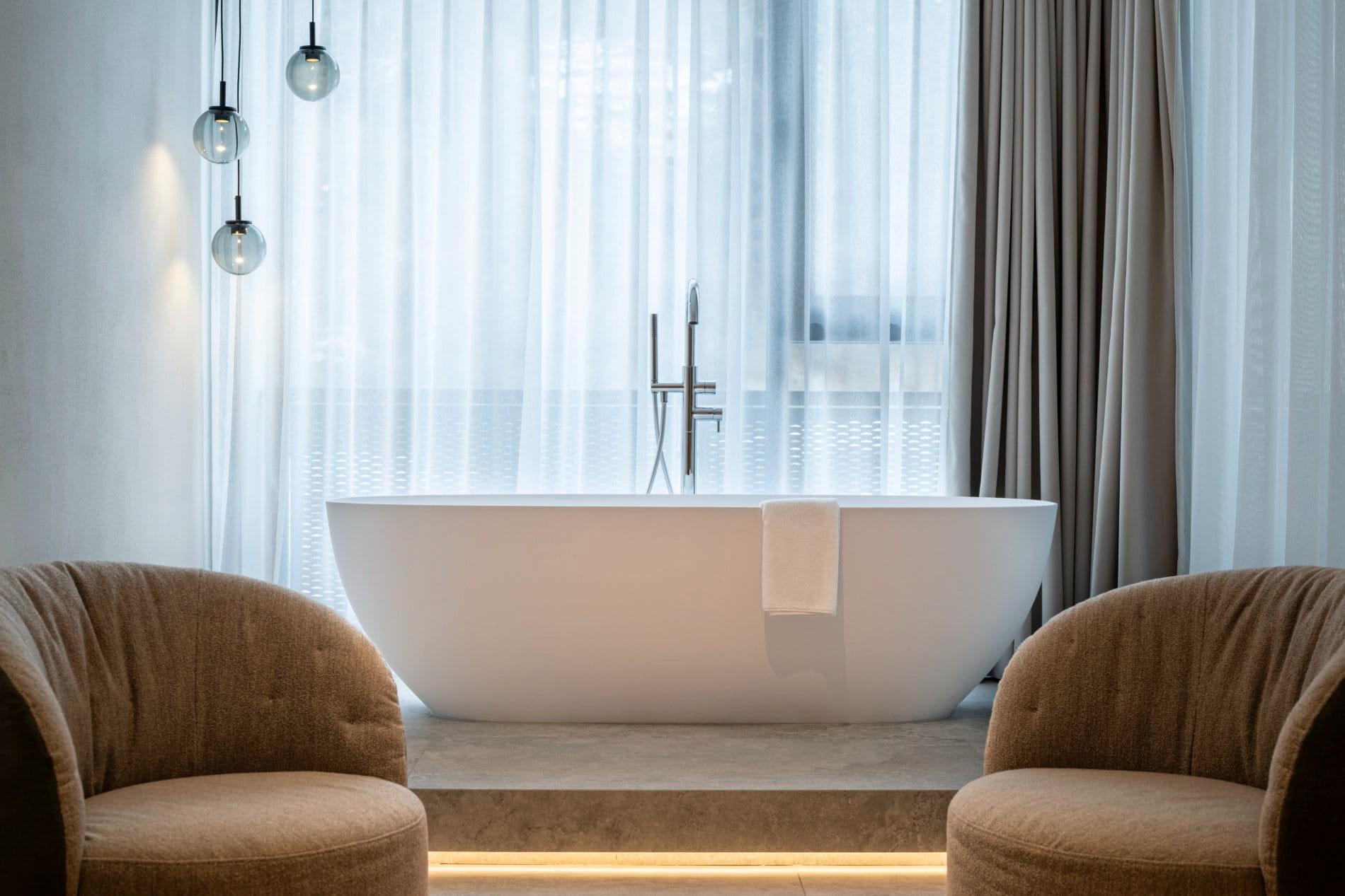 Elegante Suite mit freistehender weißer Badewanne, Designersesseln und Glaspendelleuchten.