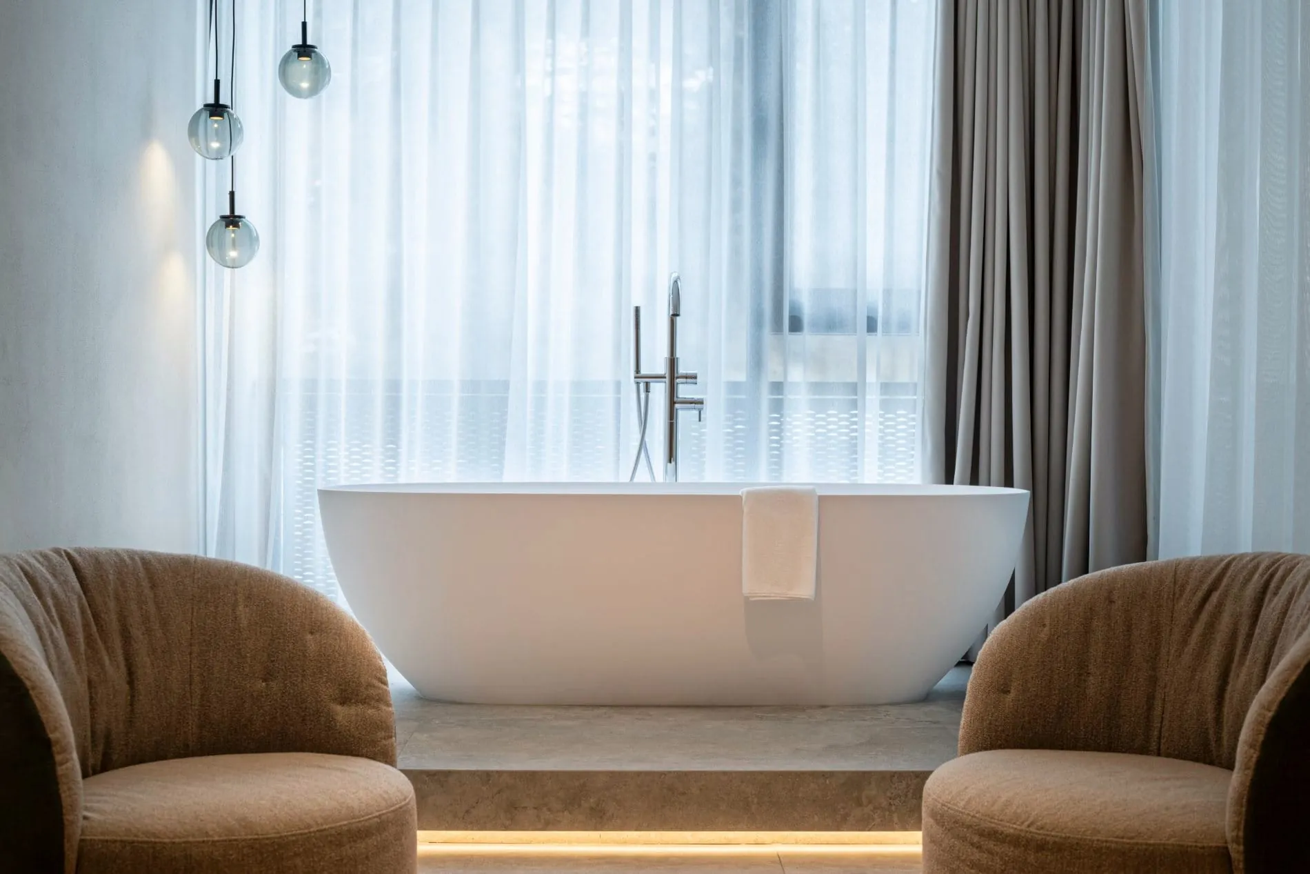 Elegante Suite mit freistehender weißer Badewanne, Designersesseln und Glaspendelleuchten.