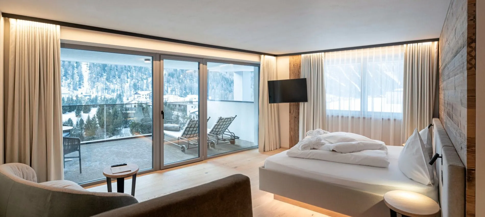 Helle Suite mit Doppelbett, Sitzecke, Terrasse mit Liegestühlen und Bergpanorama.