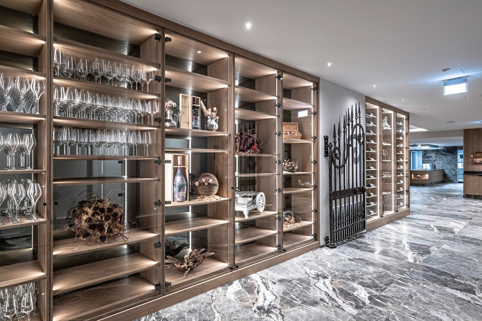 Hotelweinkeller mit Holzregalen, Glasvitrinen voller Weingläser und Marmorboden.