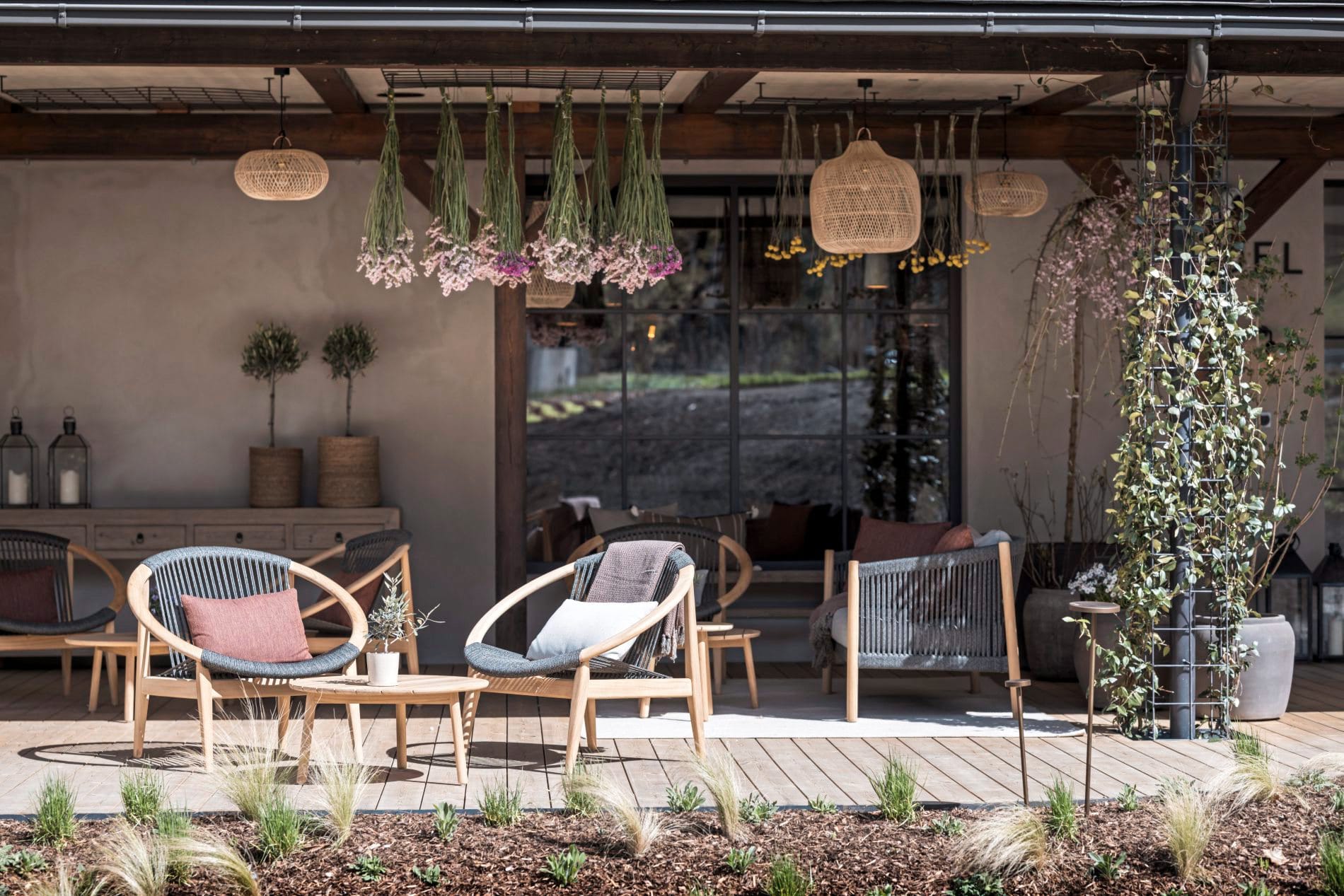 Überdachte Terrasse mit Lounge-Sesseln, hängenden Trockenblumen und Rattanleuchten.