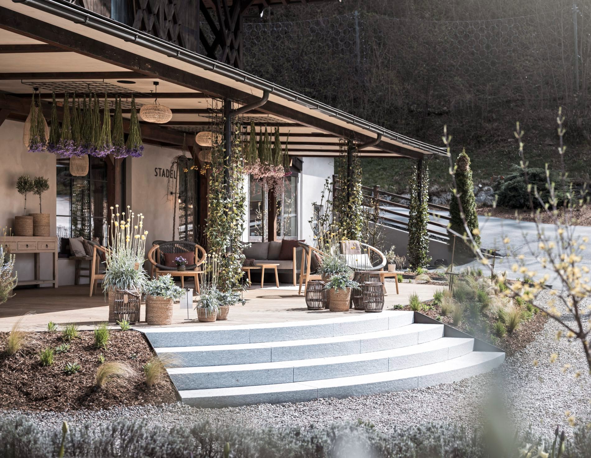 Überdachte Terrasse vor historischem Stadel mit Lounge-Möbeln und Pflanzendekoration.