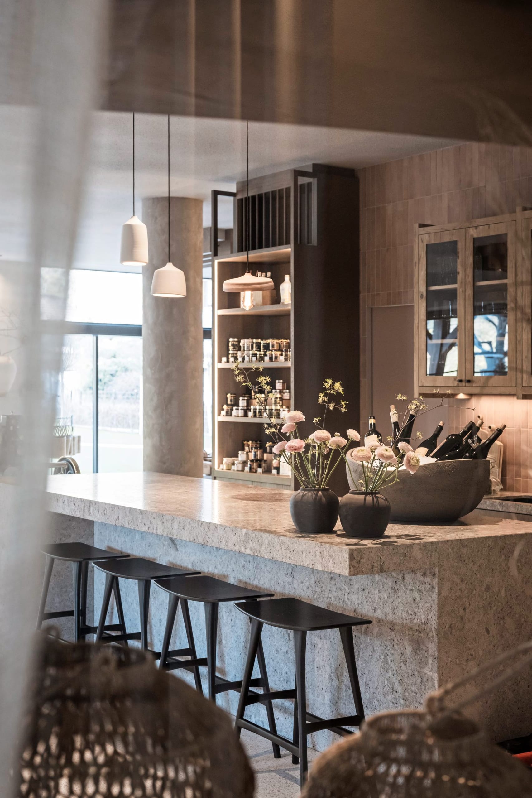 Steintresen mit schwarzen Barhockern, Pendelleuchten und Blumendekoration.