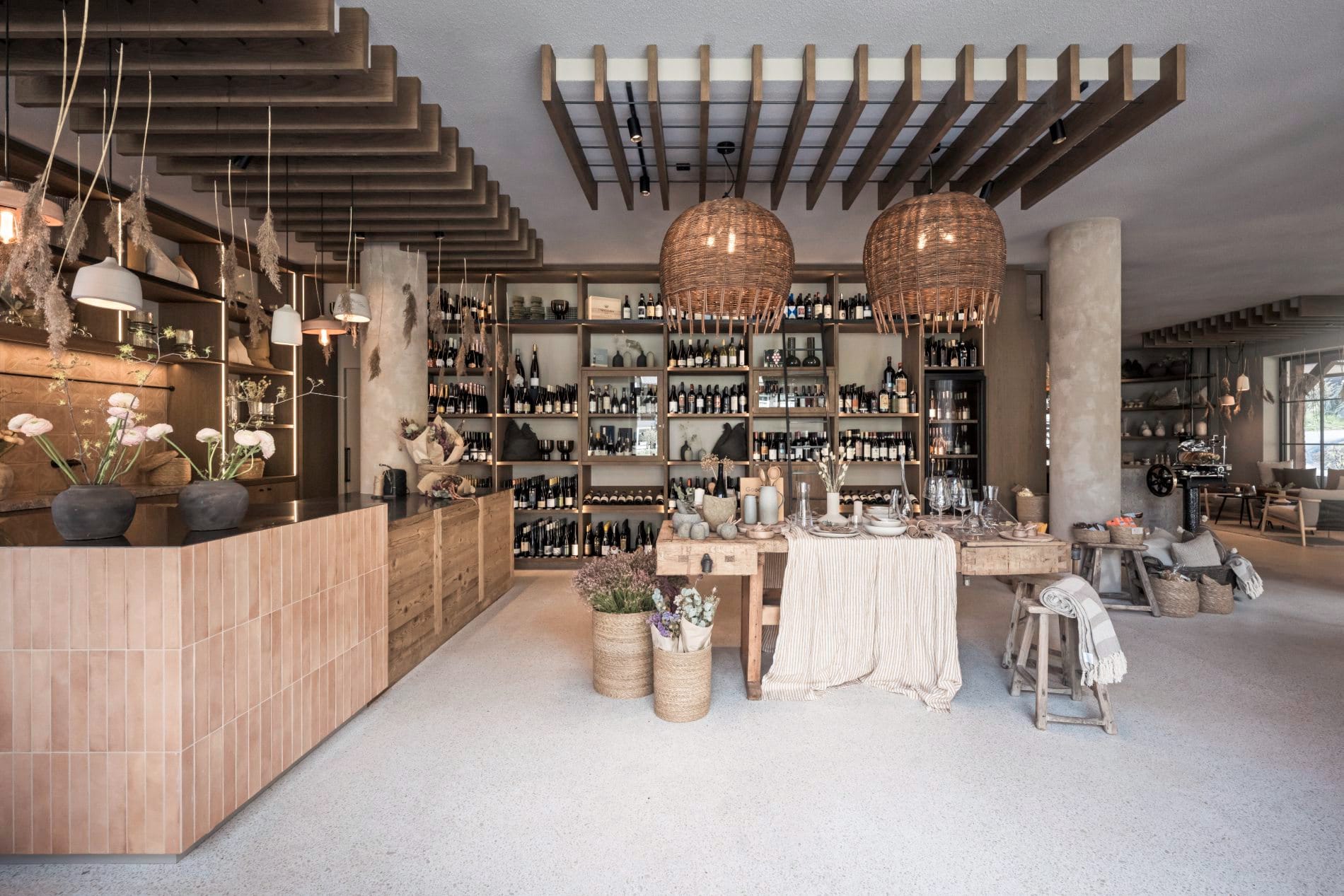 Hohe Weinregale mit Flaschen, Rattanleuchten, Dekotisch mit Geschirr und Textilien.