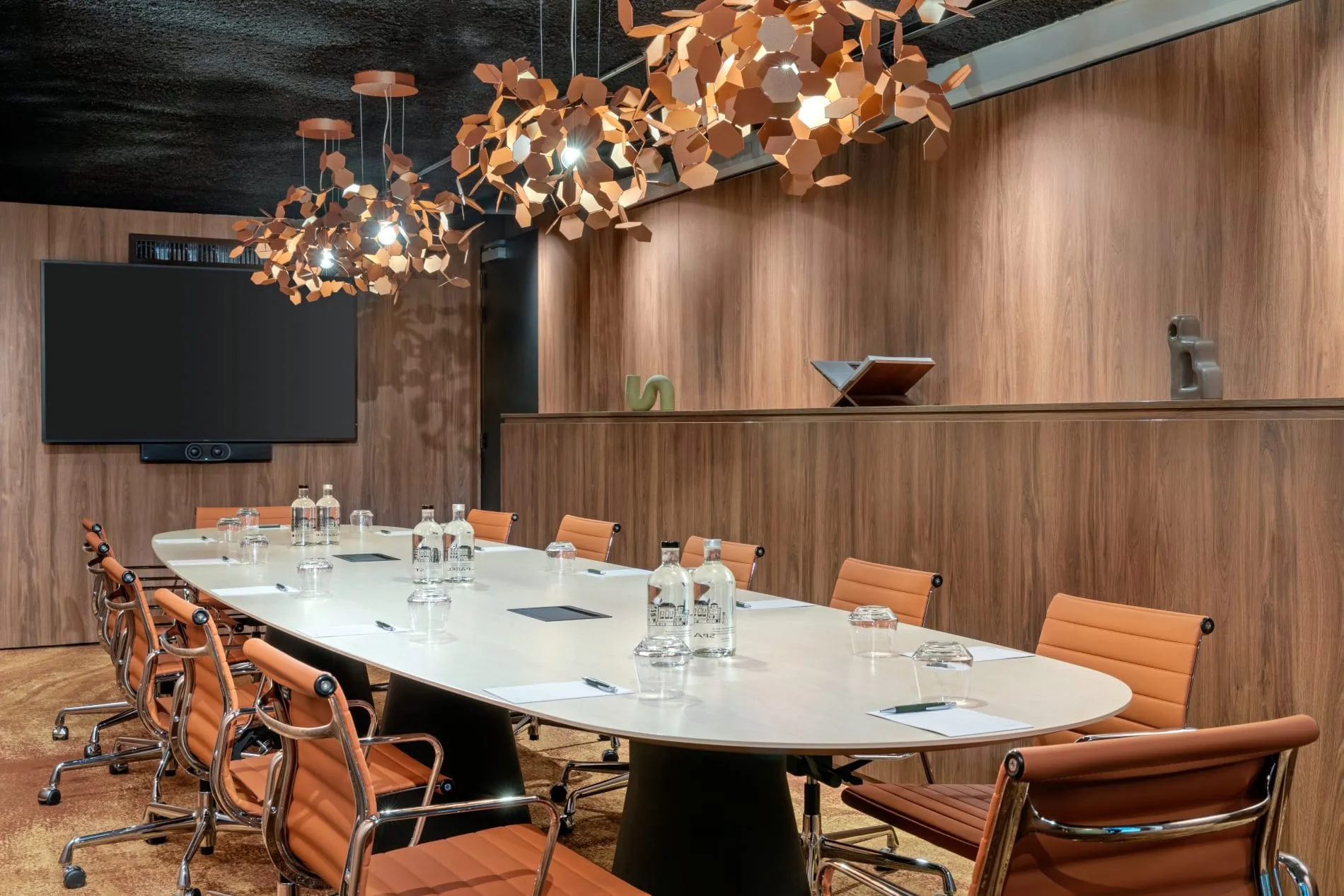 Eleganter Konferenzraum mit langem Tisch, orangefarbenen Lederstühlen und kupferner Designerleuchte.