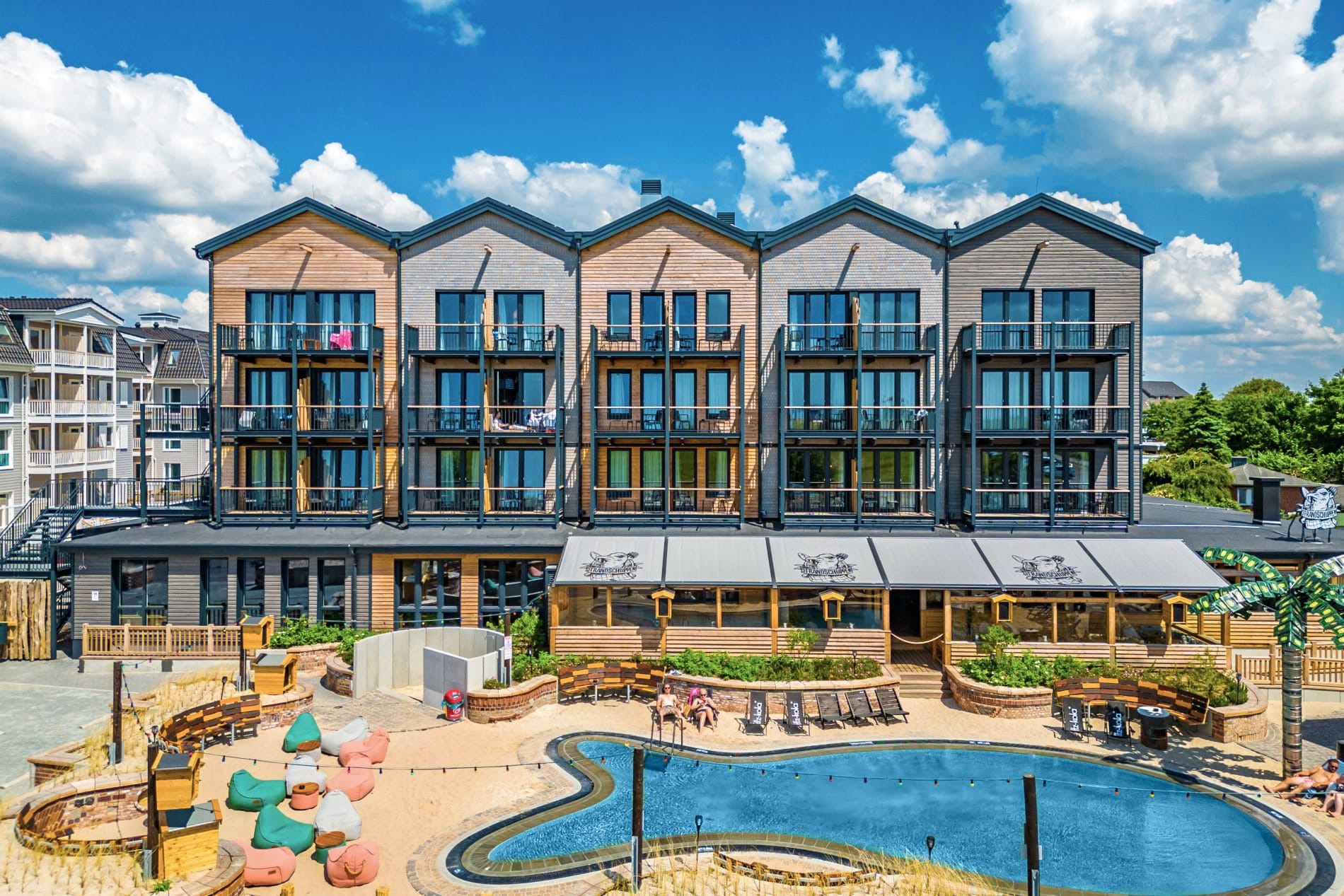 Der Außenpool „Fishbowl“ in der Bretterbude Büum ist als Beachclub-Konzept angelegt – mit Sandflächen, Palmen und einer Poolbar. Von Ostern bis Oktober können Gäste den Pool zum Schwimmen nutzen, begleitet von Veranstaltungen wie einer Pink-Poolparty oder einer Silent-Disco. In der Herbstsaison wird das Becken umfunktioniert: Ohne Wasser dient es als Skatepool.