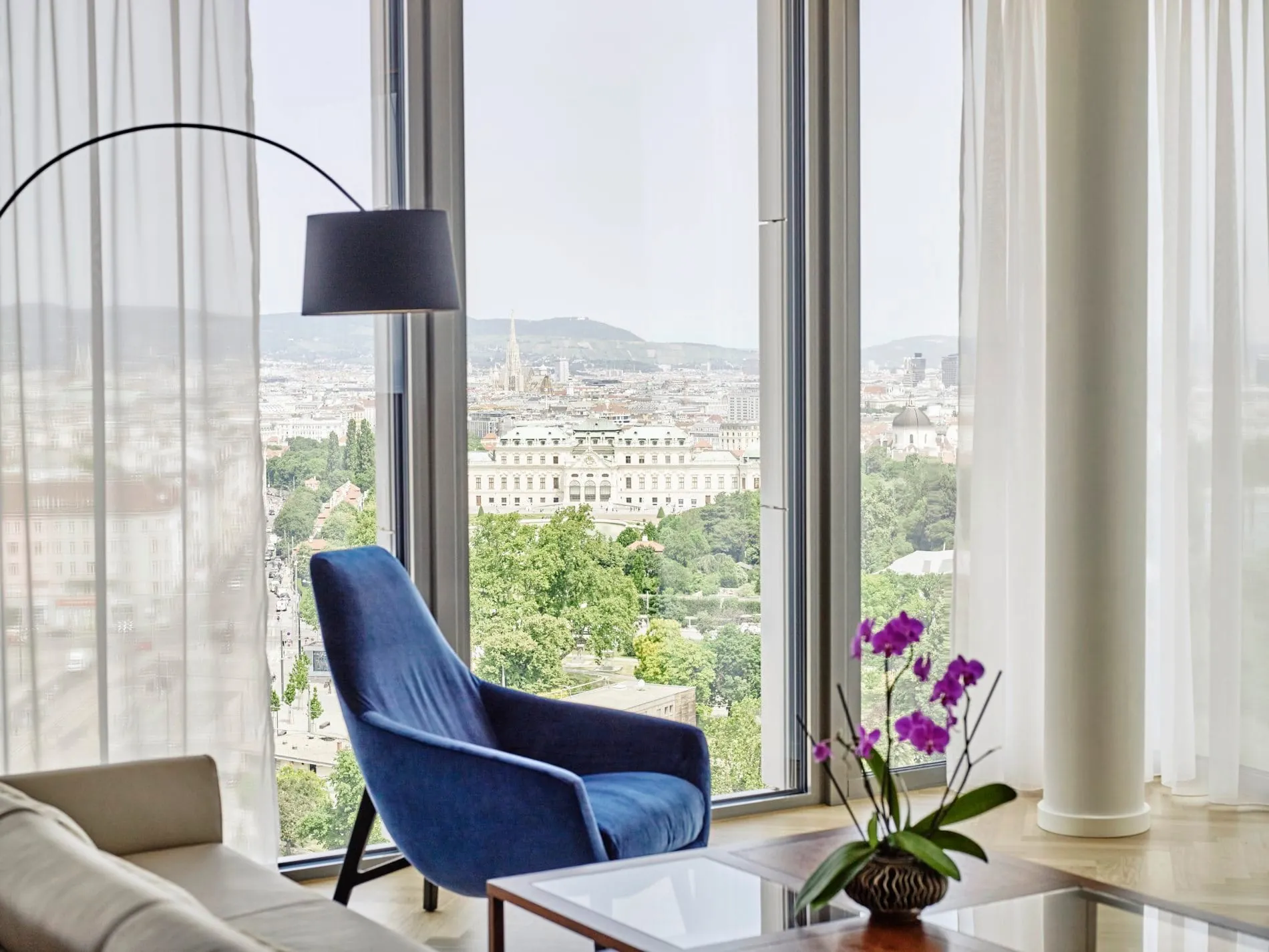 Executive Suite mit blauem Sessel und Panoramablick auf Wien und Schloss Belvedere.