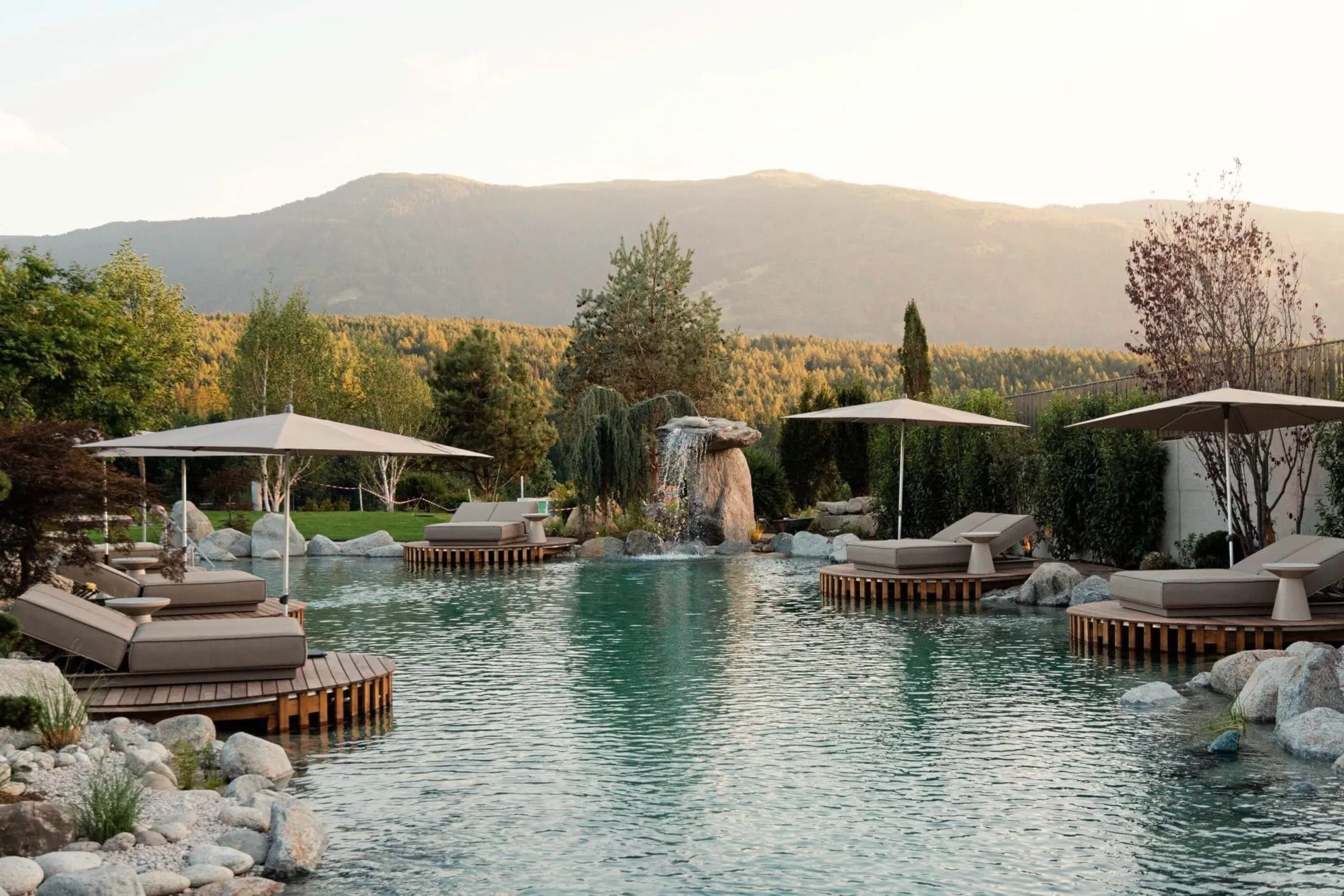 Der Naturbadeteich im Spa-Garden des Hotels Solvie in Pfalzen wird durch Daybeds, eine Yogaplattform und Blick auf die umliegende Landschaft ergänzt.