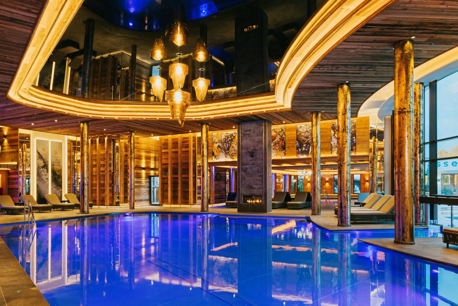 Der 140 Quadratmeter große Innenpool des Ortner's Resorts in Bad Füssing ist mit Thermalwasser aus der hauseigenen Quelle gefüllt, das auf 37 Grad temperiert ist. Die Gestaltung umfasst goldene Säulen, eine Spiegeldecke, Muranolüster, Altholz und einen Kamin.