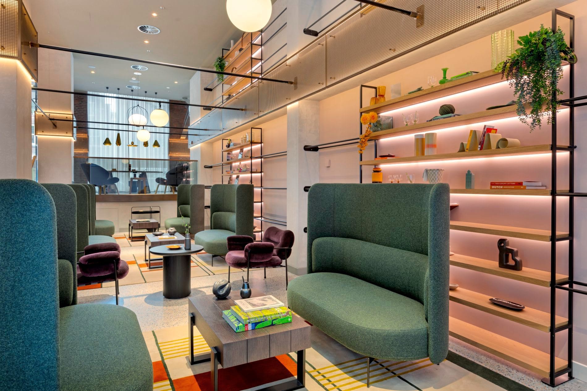 Moderne Hotellobby mit grünen Sesseln, beleuchteten Wandregalen und gemütlichen Sitzgruppen.