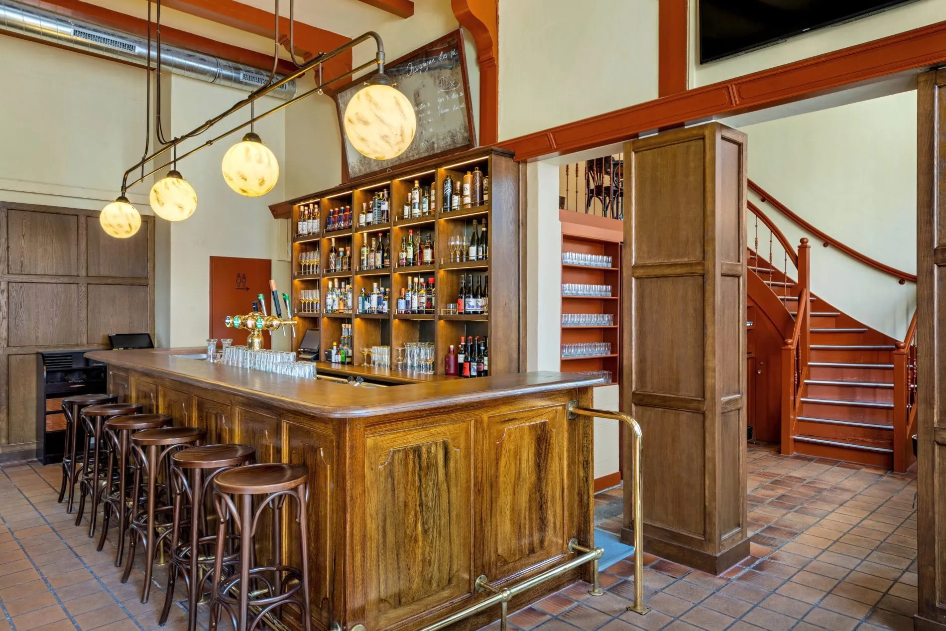 Klassische Hotelbar mit Holztresen, Barhockern, Spirituosenregal und runden Pendelleuchten.