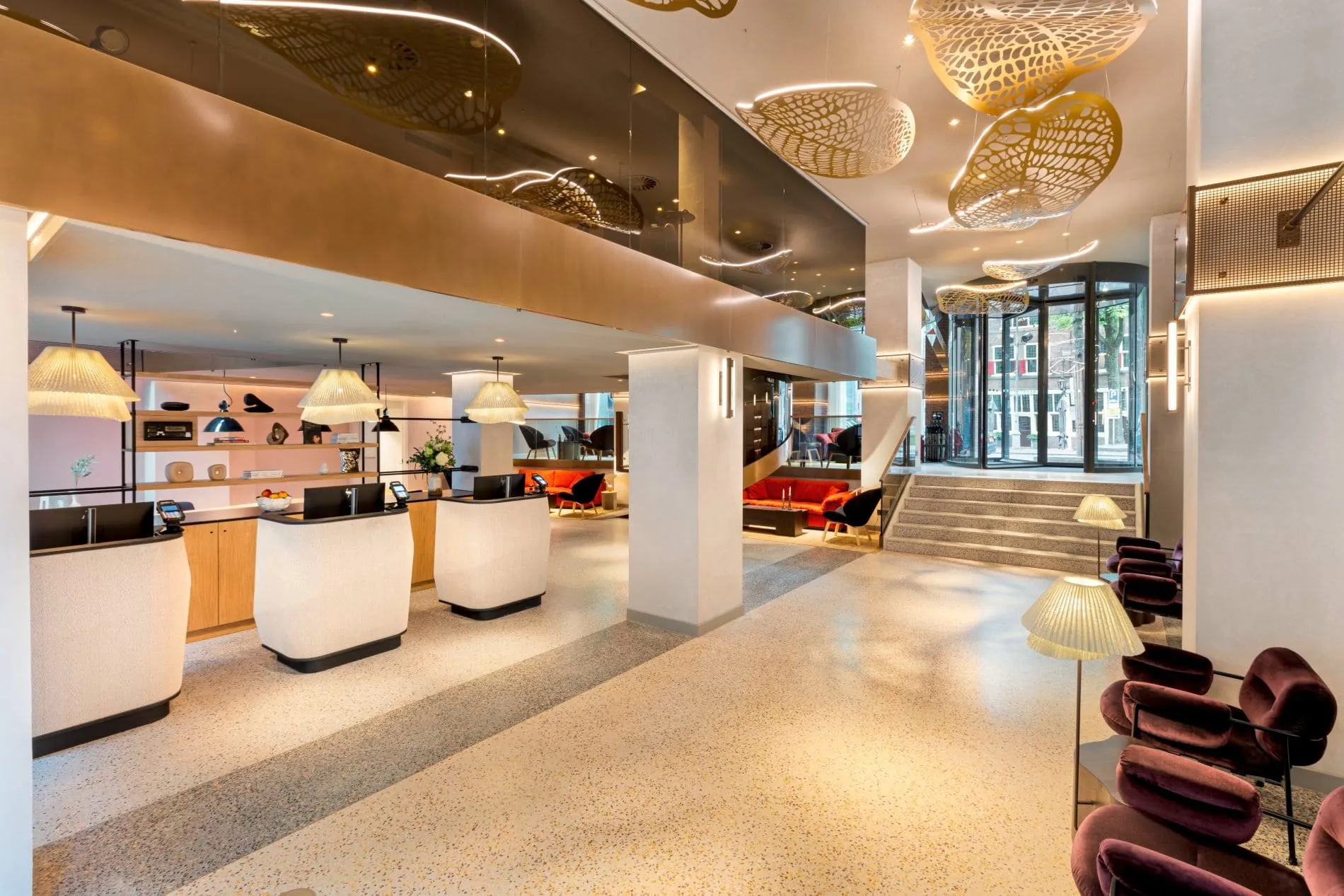 Moderne Hotellobby mit Empfangstresen, goldenen Deckenskulpturen, Terrazzoboden und Glaseingang.