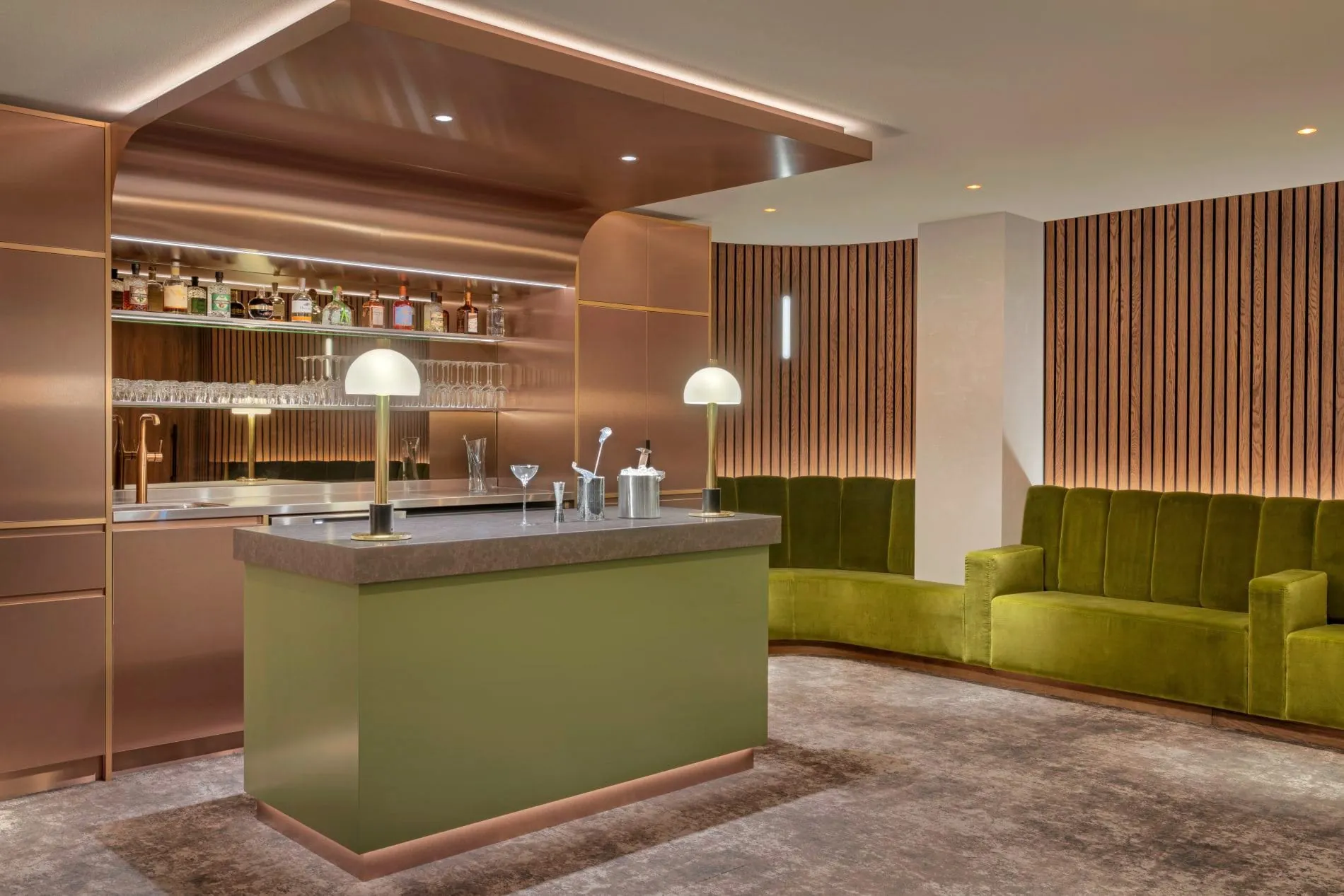 Elegante Hotelbar mit Kupferverkleidung, grünem Samtsofa, Holzlamellen und Cocktailzubehör.