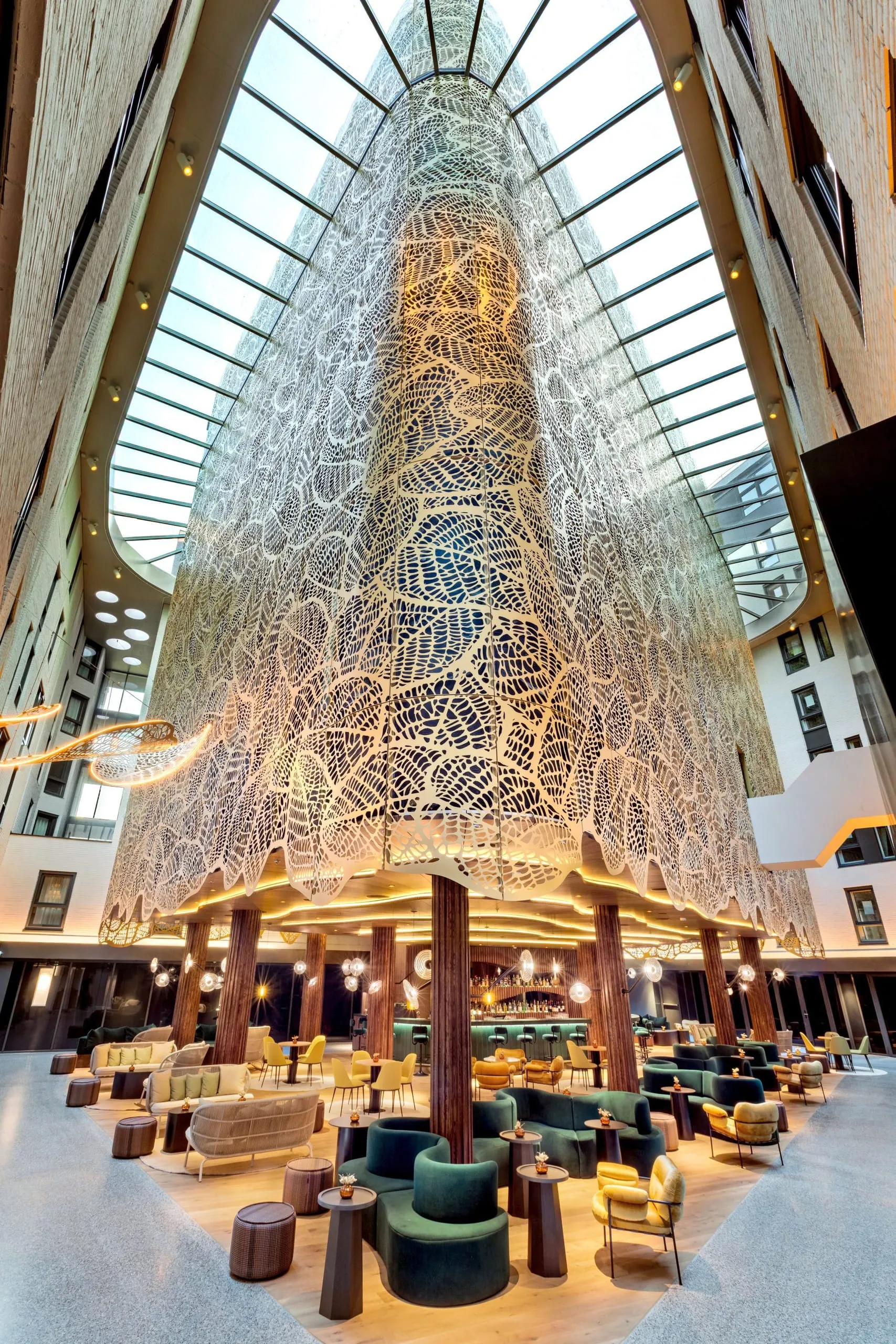 Mehrstöckiges Hotelatrium mit riesiger beleuchteter Netzskulptur, Bar und bunten Sesseln.