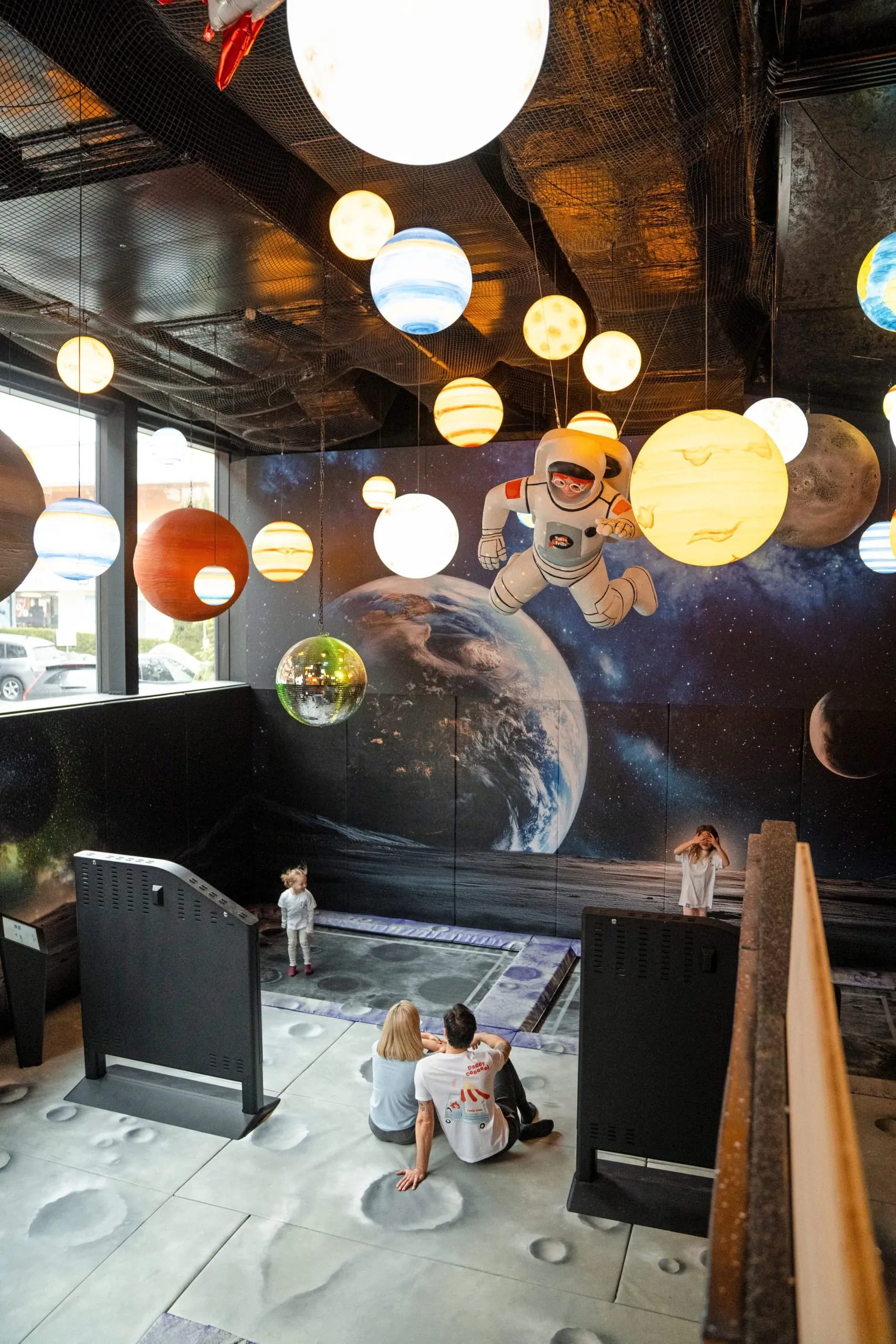 Weltraum-Spielbereich mit leuchtenden Planeten, Astronautenfigur, Trampolin und spielenden Kindern.
