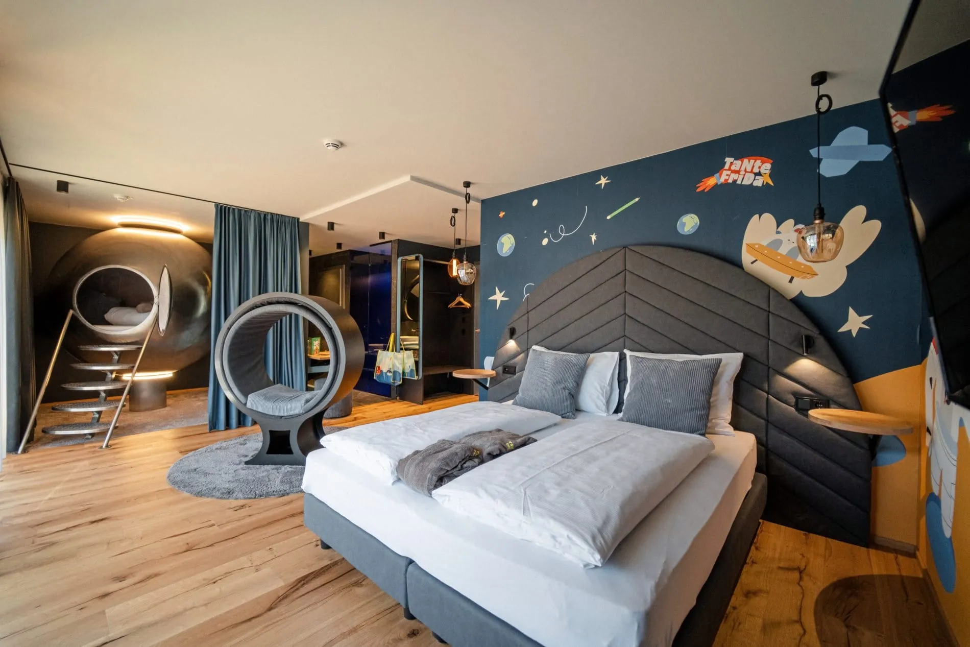 Space Themenzimmer mit Weltraum-Wandgestaltung, grauem Doppelbett und Kinderschlafkapsel.