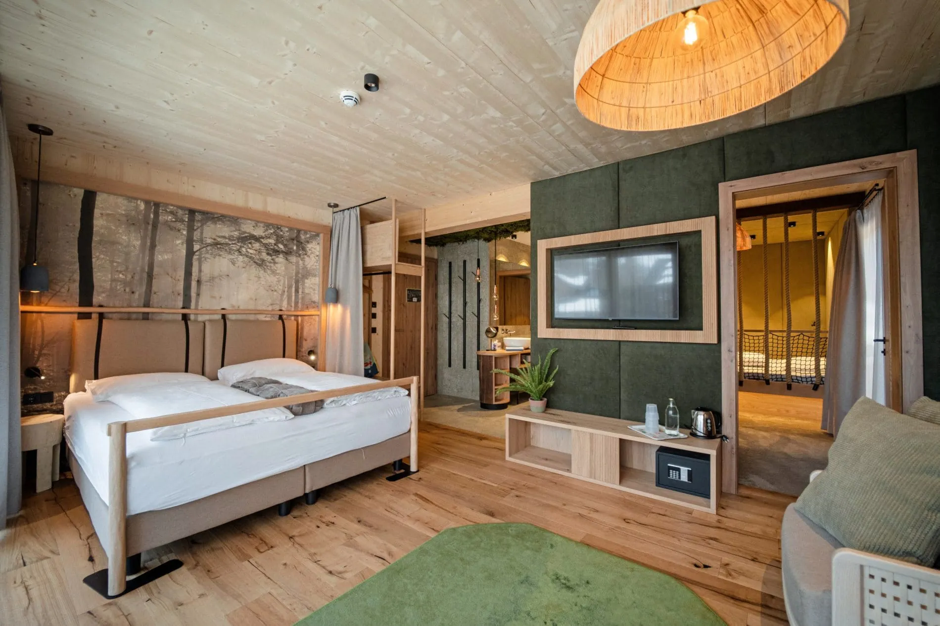 Nature Hotelzimmer mit Holzdecke, Waldtapete, Doppelbett und separatem Kinderschlafbereich.