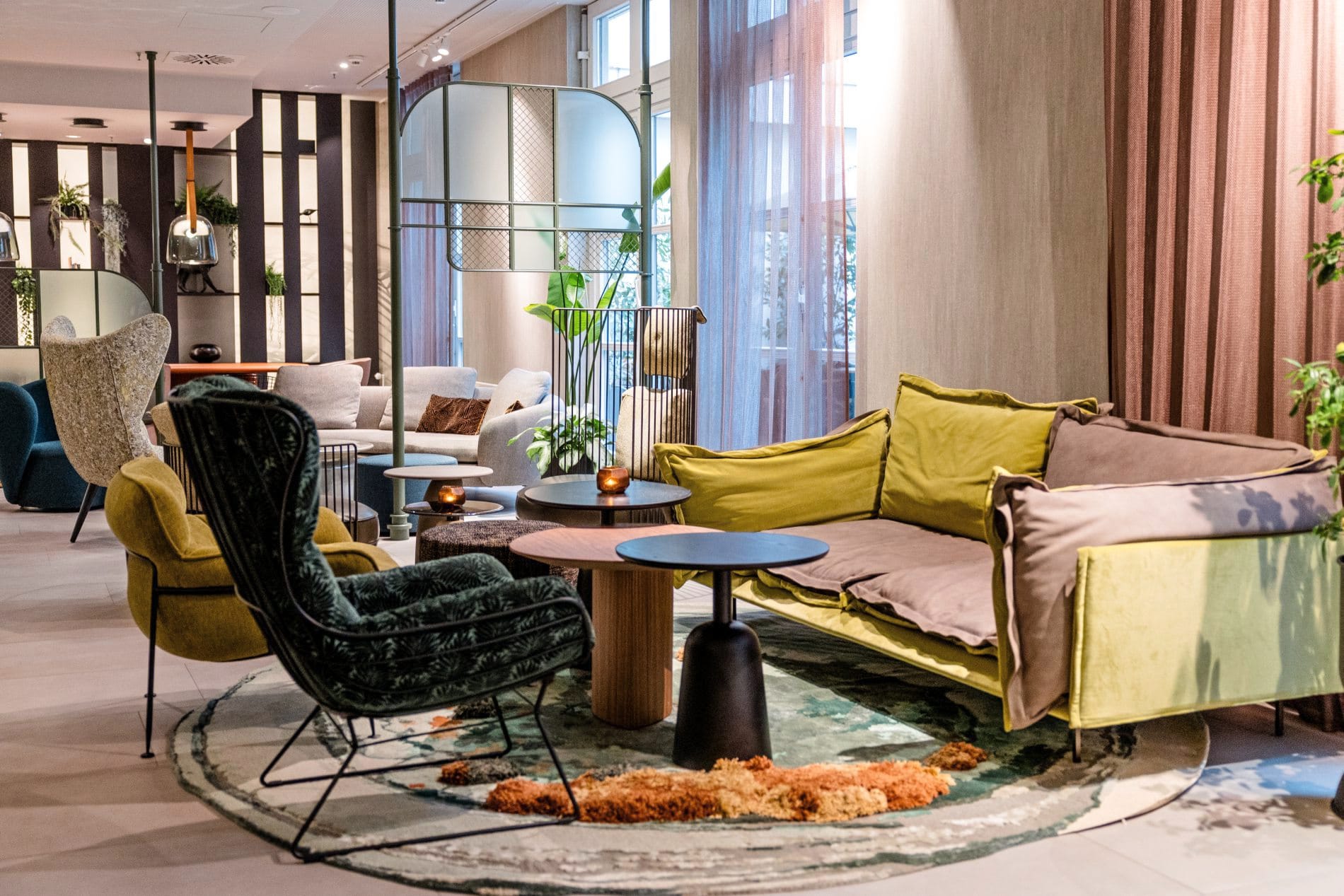 Lounge im Motel One Frankfurt mit bunten Sofas, Sesseln, Beistelltischen und Pflanzen.