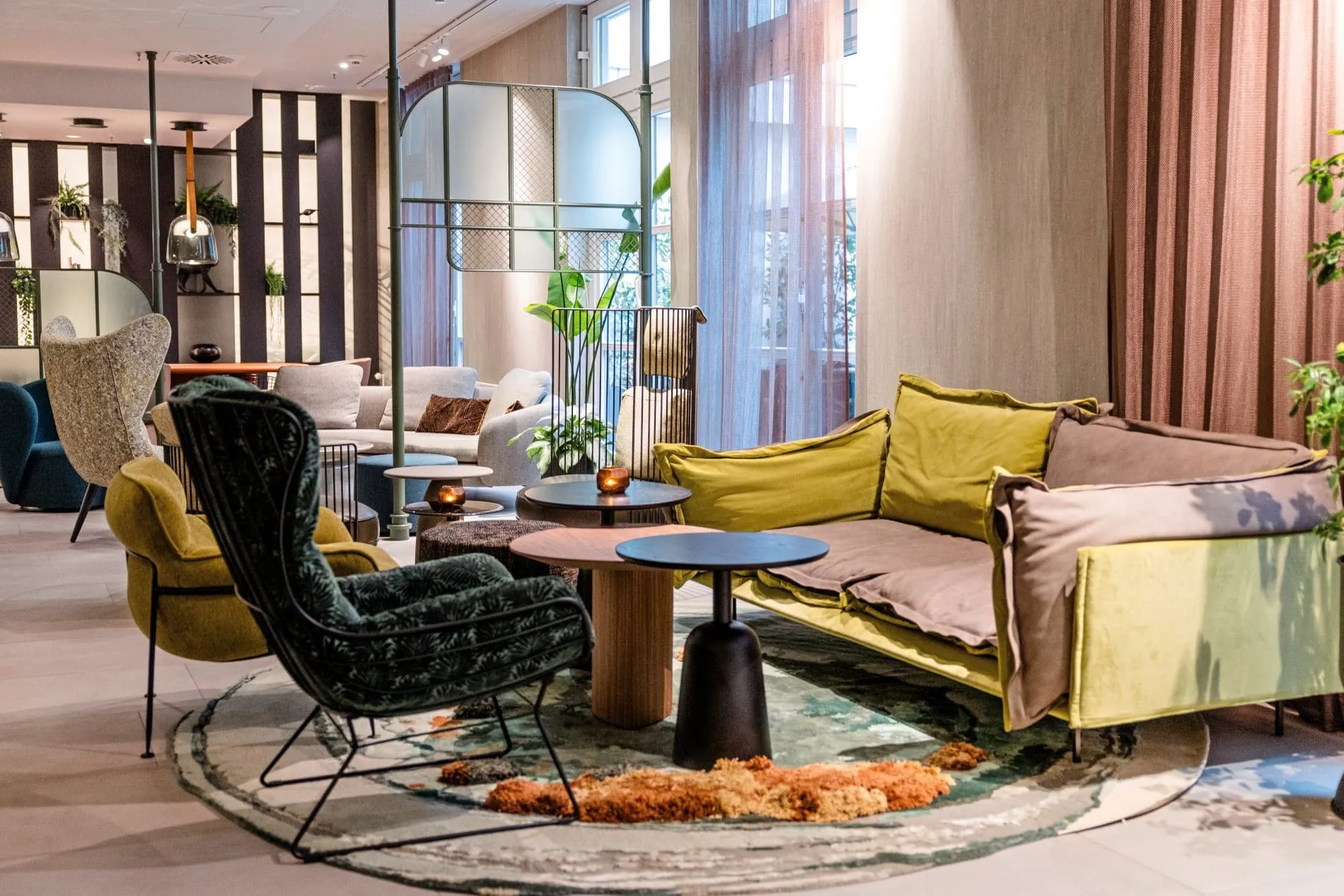 Lounge im Motel One Frankfurt mit bunten Sofas, Sesseln, Beistelltischen und Pflanzen.