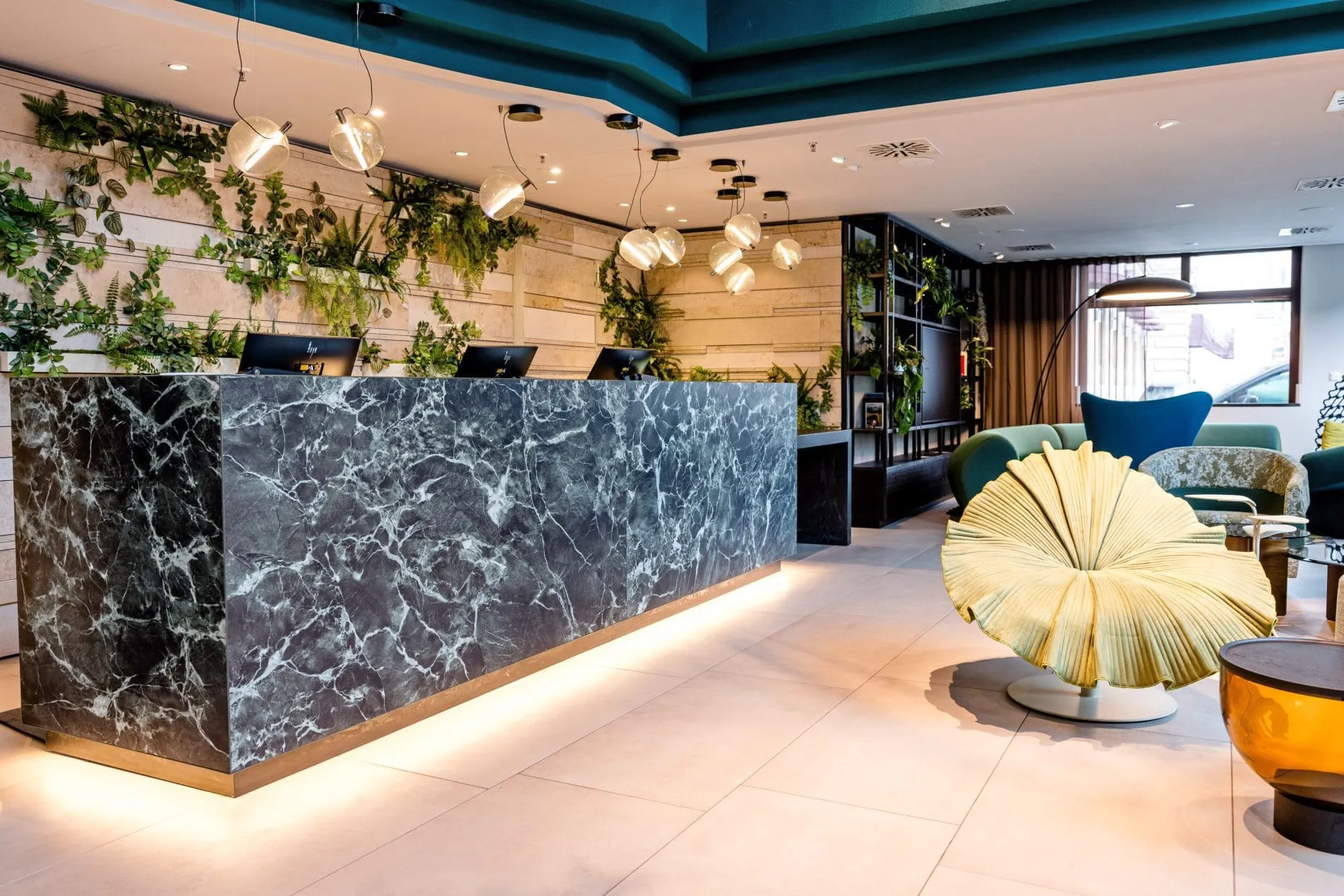 Rezeption im Motel One Frankfurt mit dunklem Marmortresen, Pflanzen und gläsernen Pendelleuchten.
