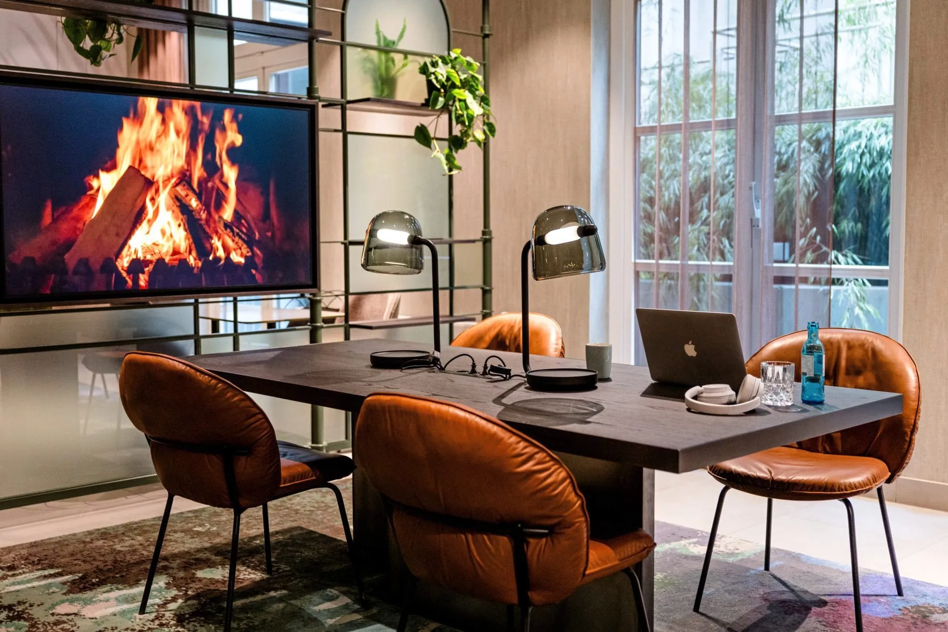 Arbeitsplatz im Motel One Frankfurt mit Laptop, Lederstühlen, Tischlampen und Kaminbildschirm.