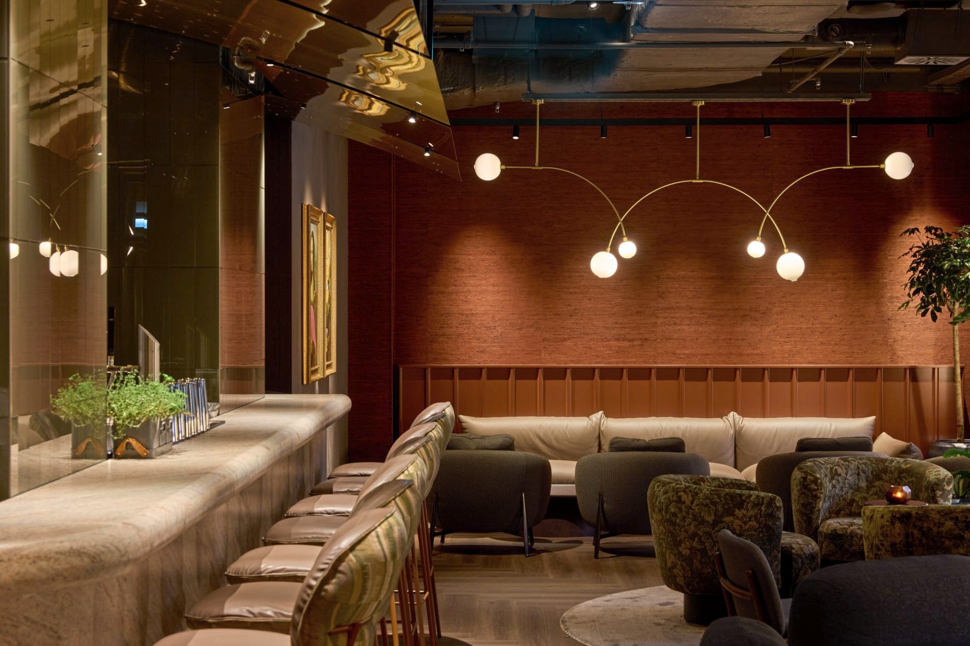 Bar-Lounge mit Marmortresen, Barhockern, Kugelleuchten an Messingbögen und gemütlichen Polstersesseln